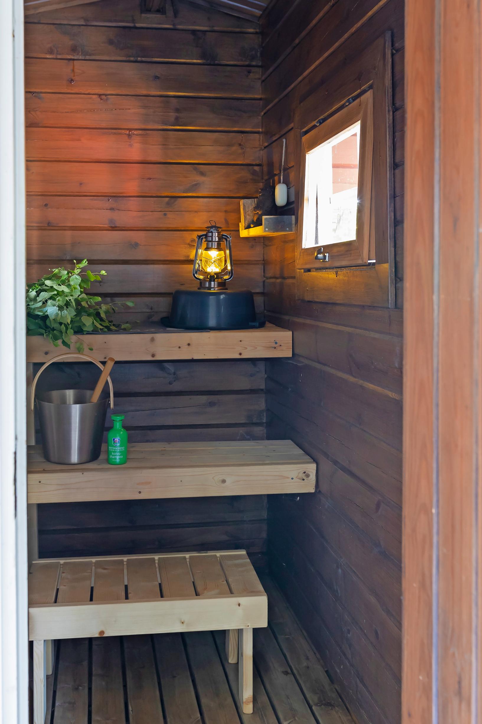 sauna benches, a lantern, a birch whisk, a wooden pail, and a window