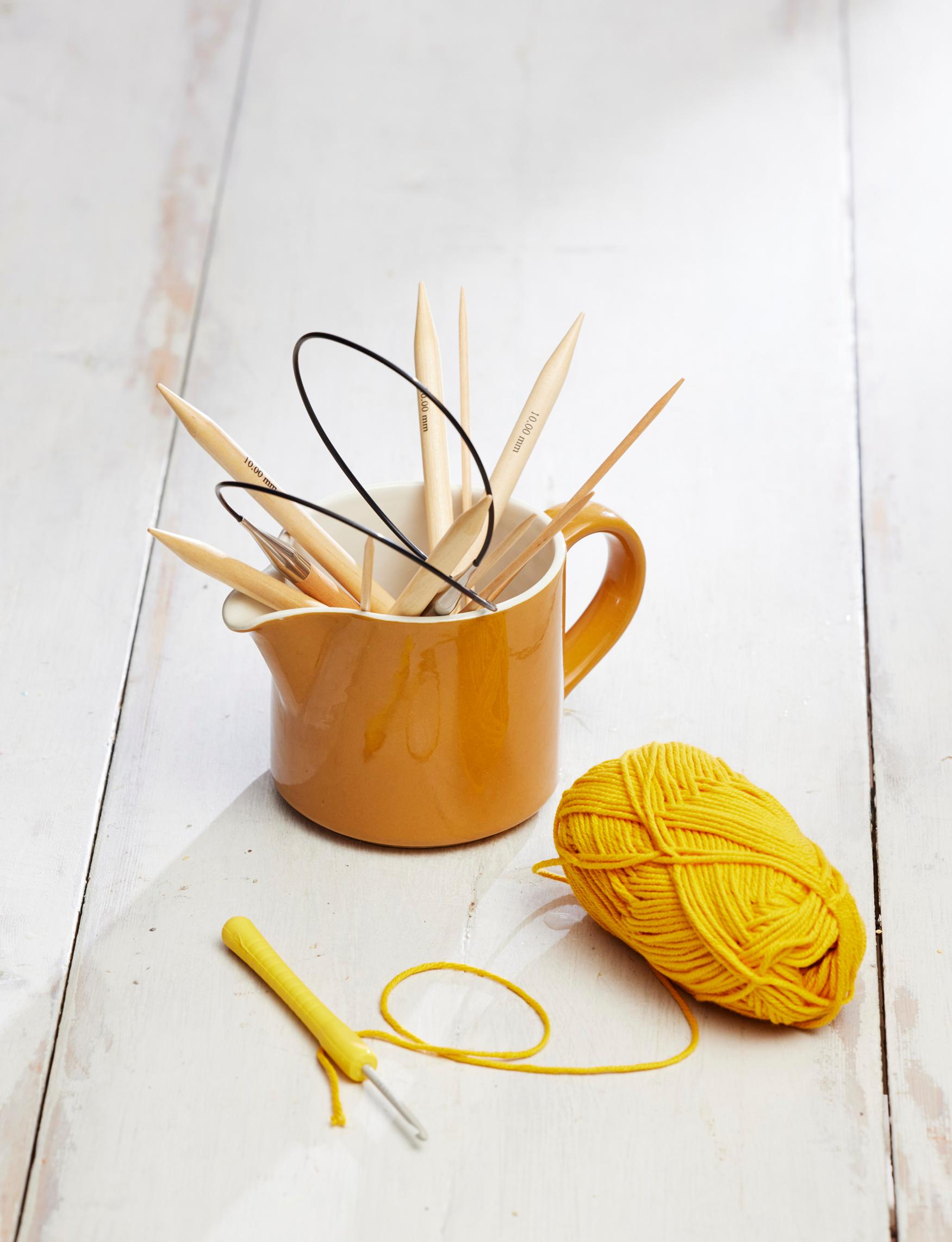 An old Arabia milk pitcher holding crochet hooks and double-pointed knitting needles.