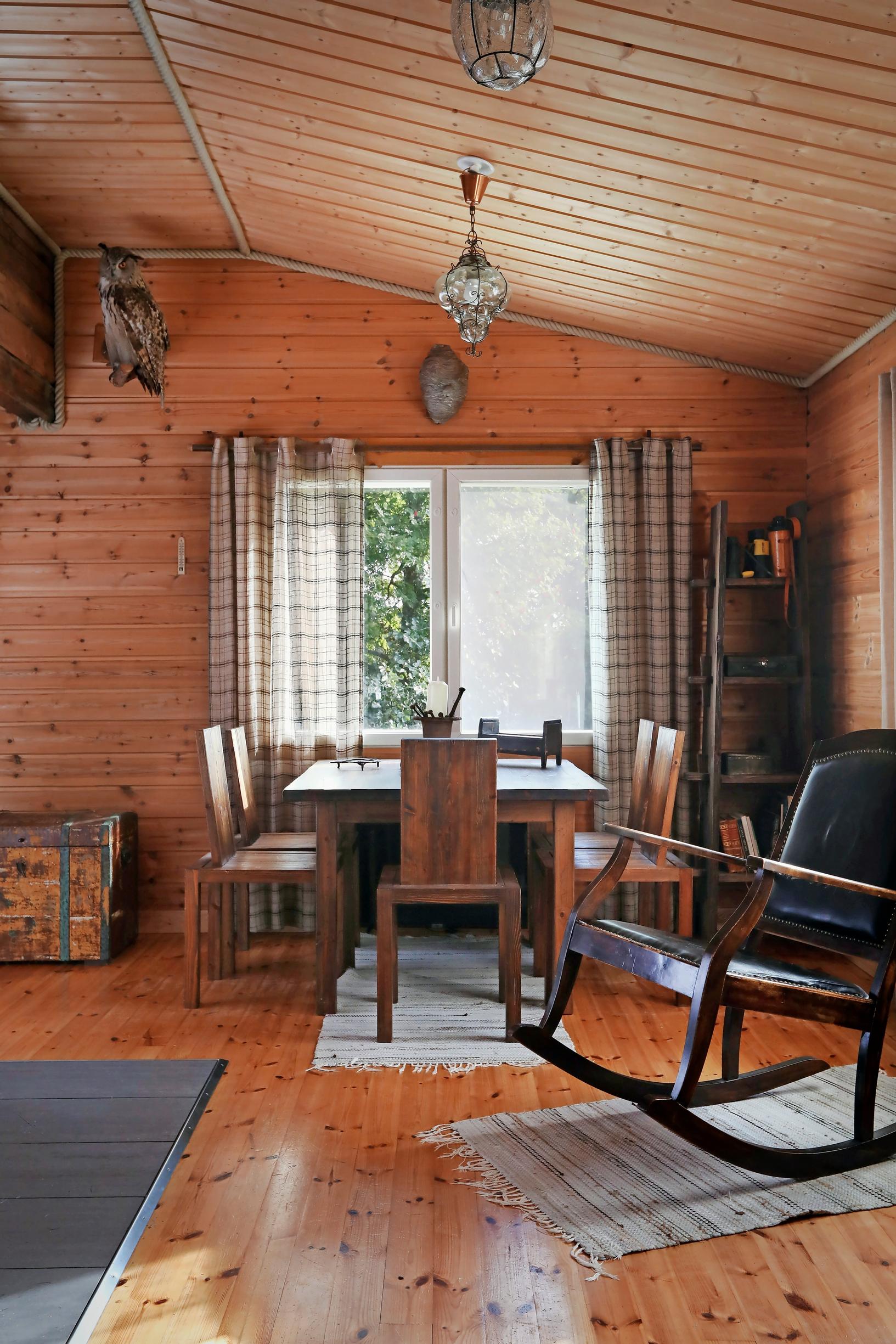 Wooden floor and walls, a rocking chair, a table set, and rag rugs.