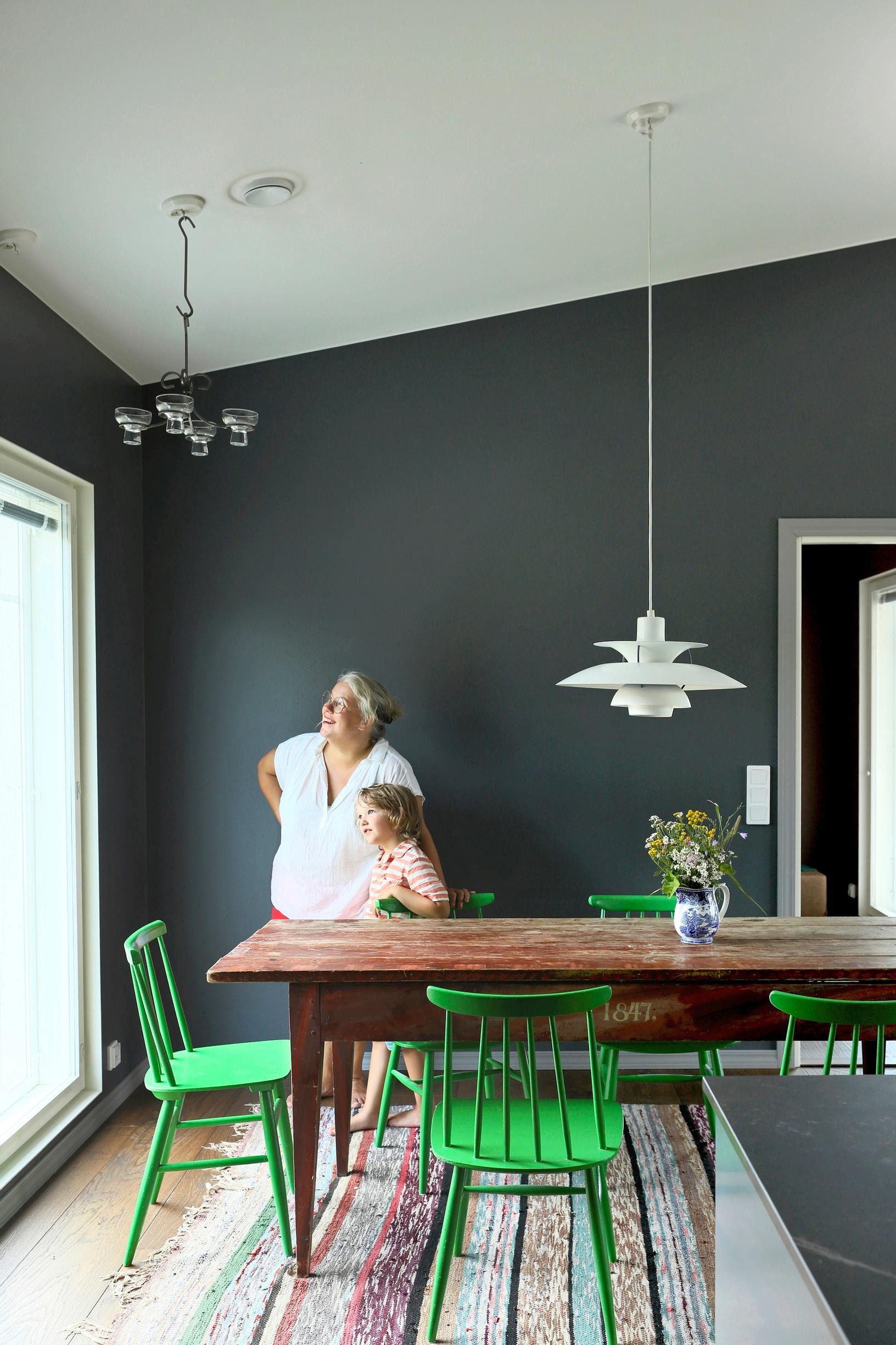 Bright green spindle-back chairs around the kitchen table. A mother and child looking out the window.