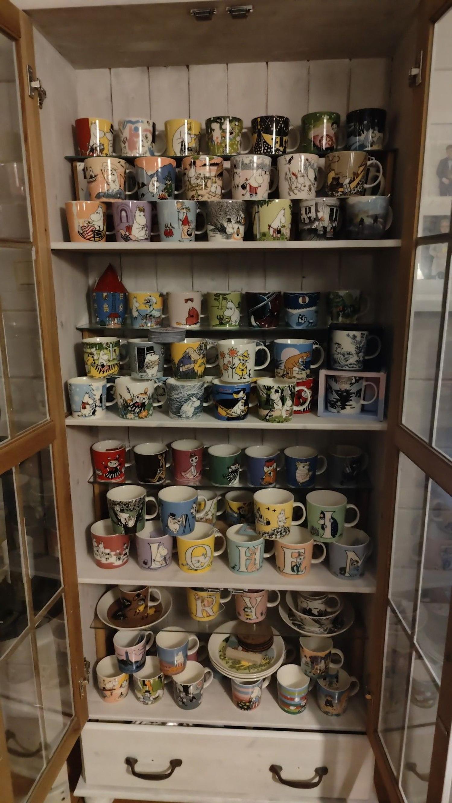 A display cabinet with doors open, filled with Moomin mugs