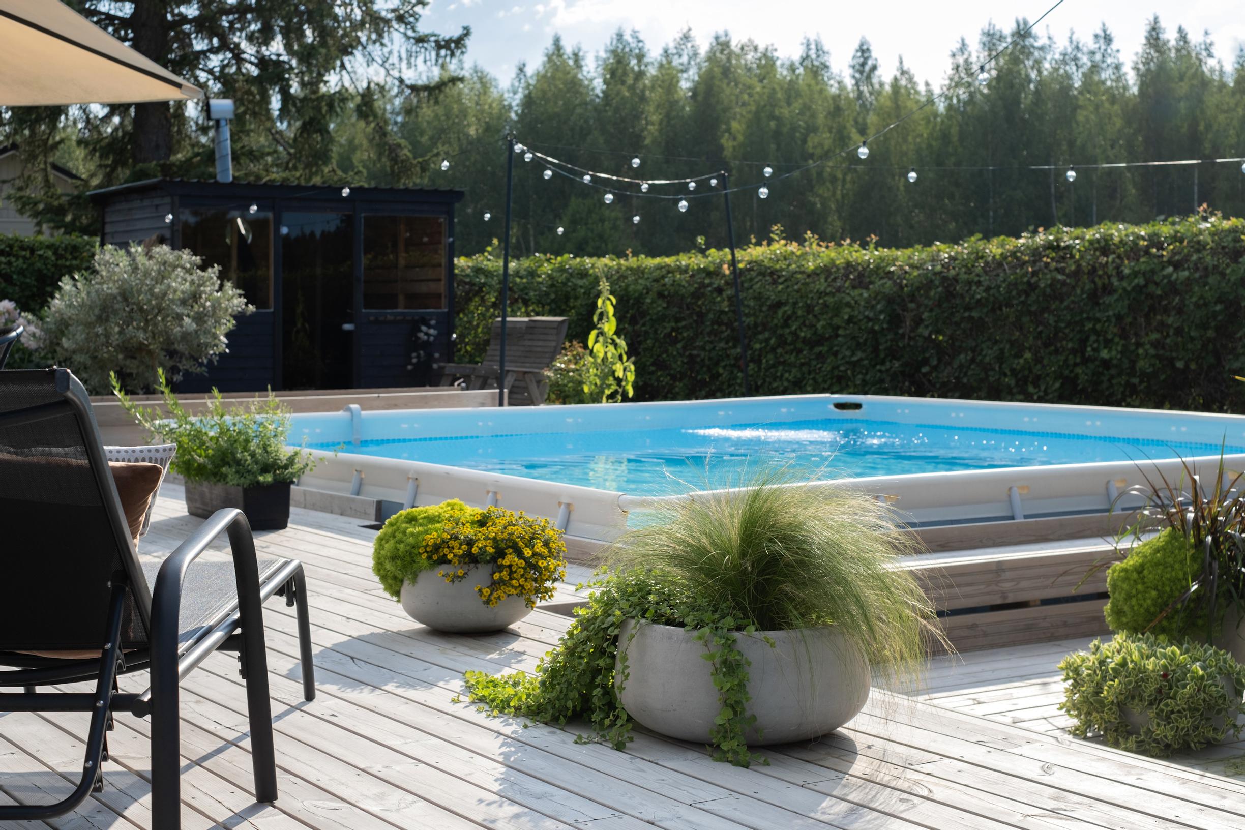 A deck built around the swimming pool. There are potted plants on the deck.