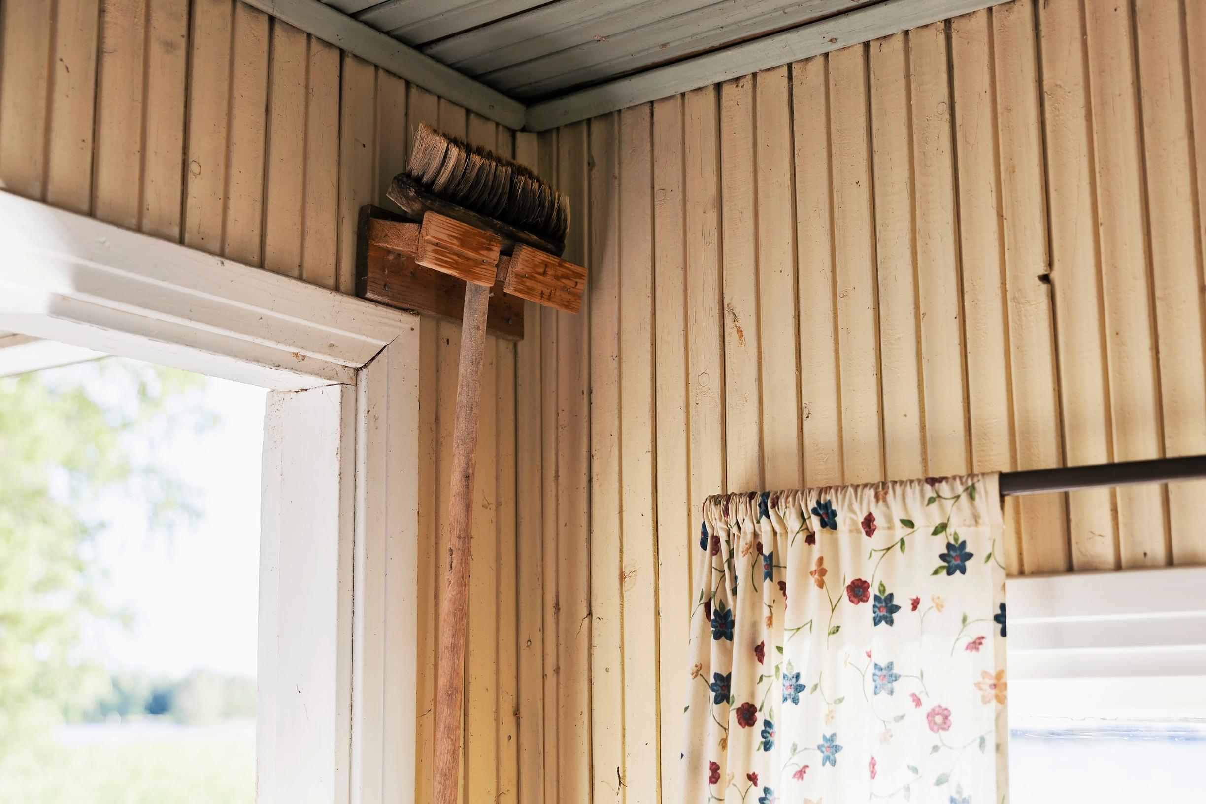 Brush hanging on a wall rack on a wooden wall, curtain rod, windows