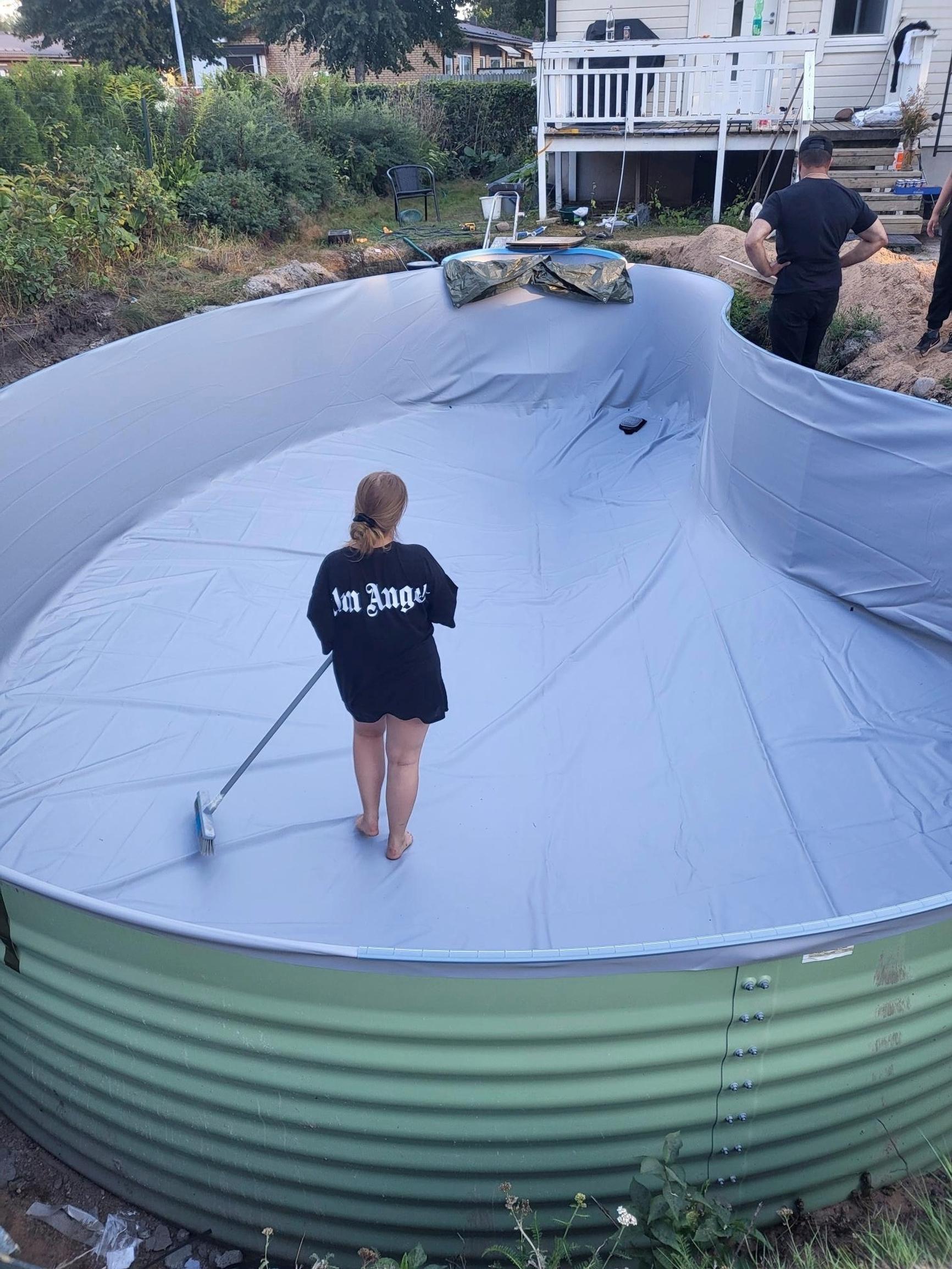 Someone smoothing out the bottom of the pool liner with a long-handled brush.