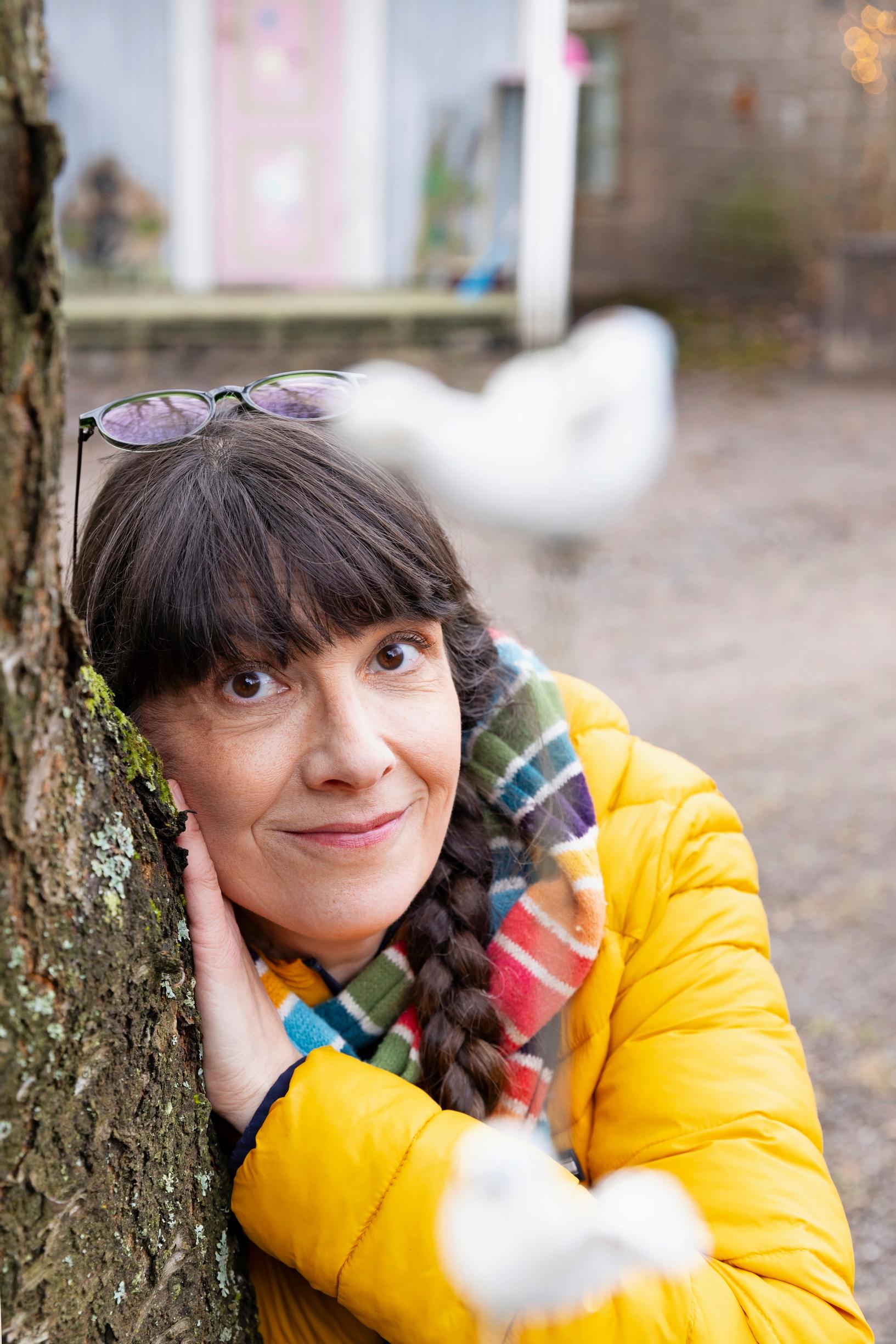 a woman in a yellow coat leaning against a tree