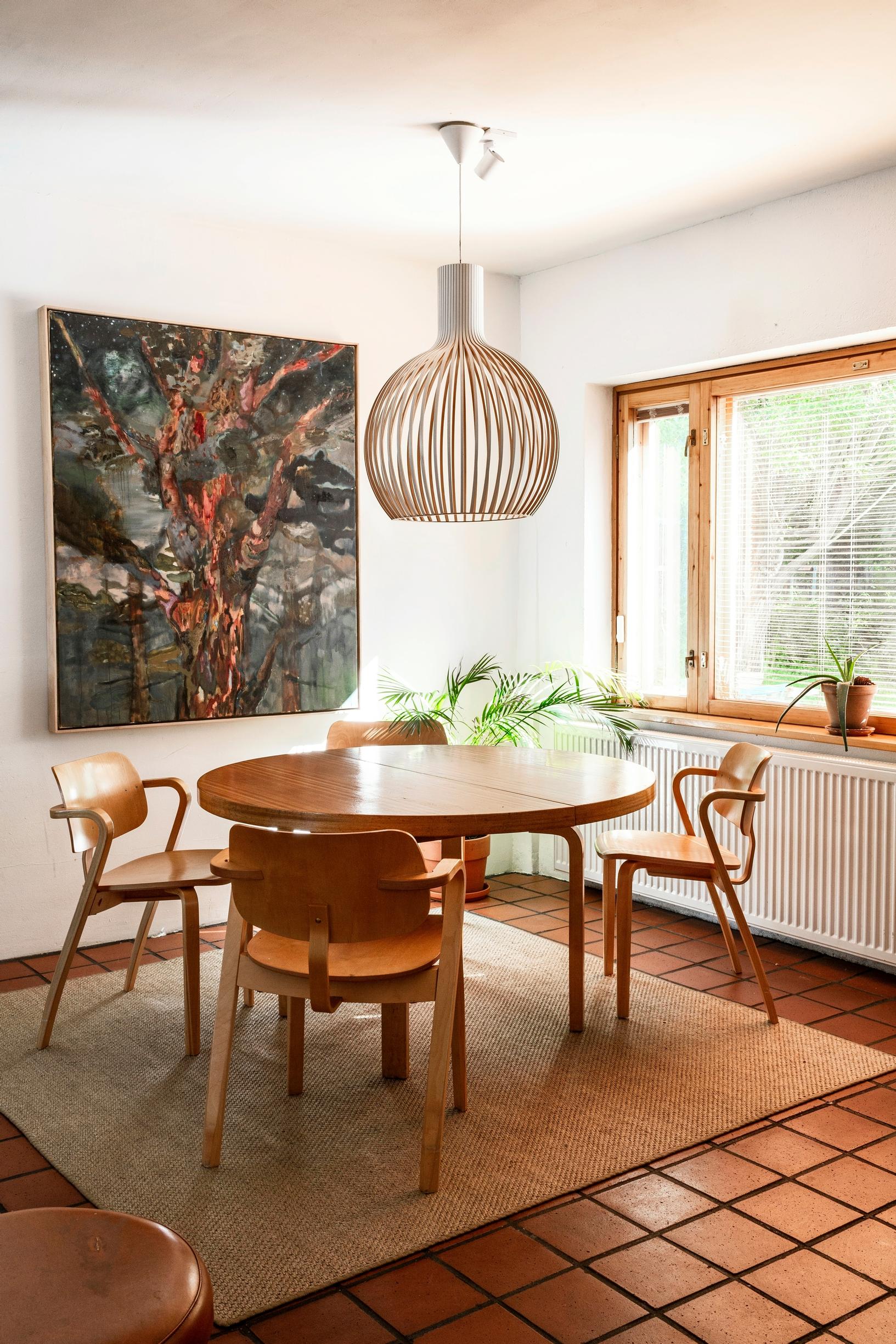 Dining table and chairs in the home converted from the Alvar Aalto heating plant, pendant light, painting, and tiled floor