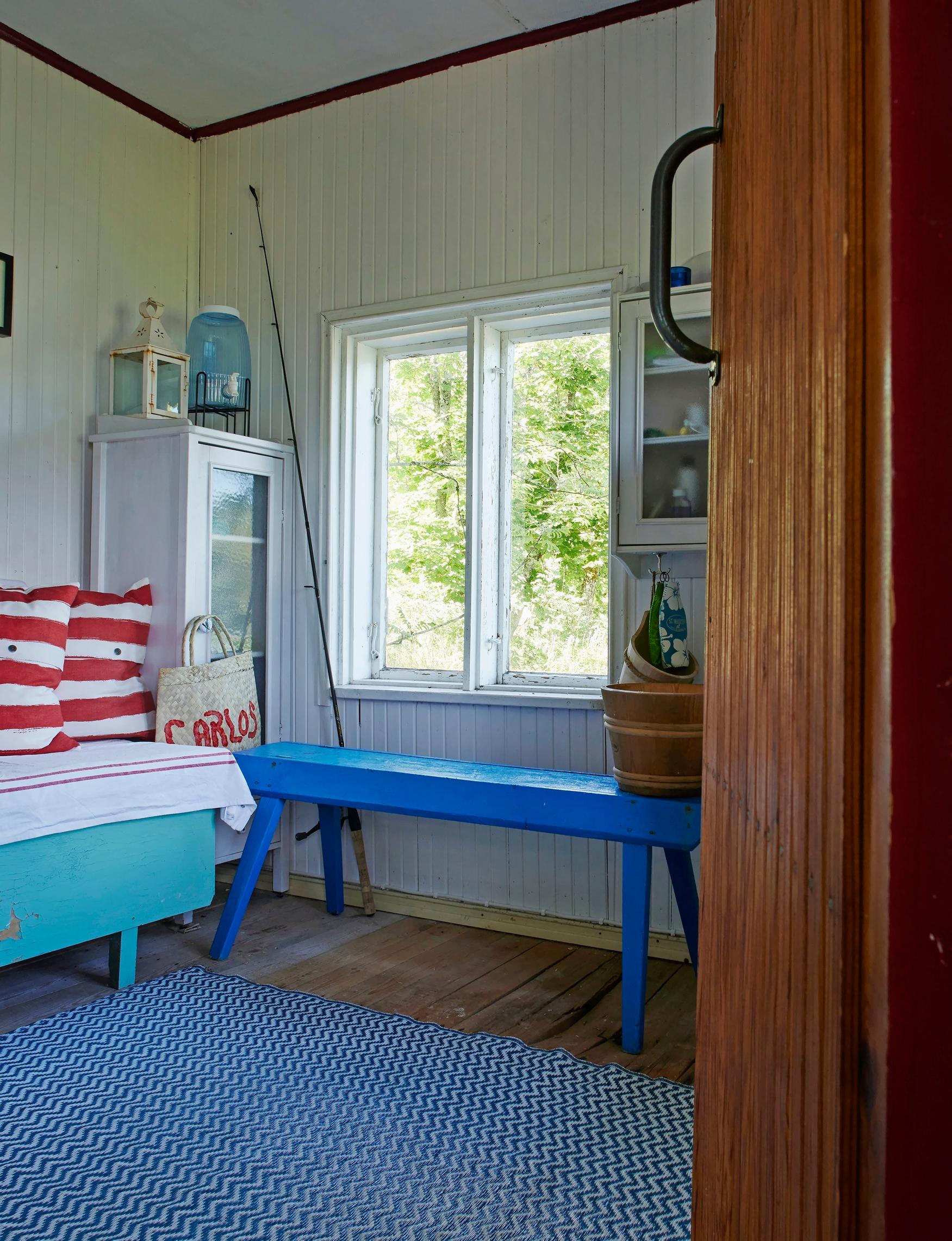 a blue bench, wooden water bucket and a turquoise bed with red‑and‑white striped pillows, window