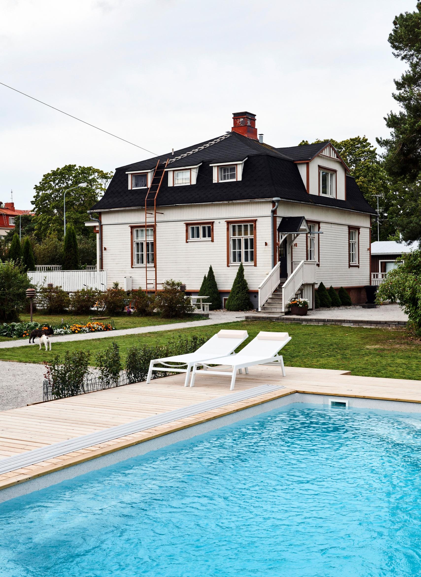 Mia and Ulla’s old white villa, with a swimming pool in the foreground and lounge chairs beside it
