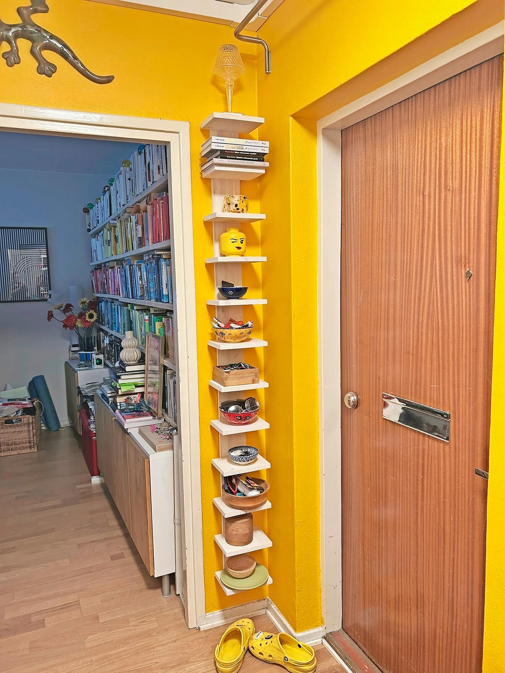 A narrow open shelf on a yellow entryway wall.