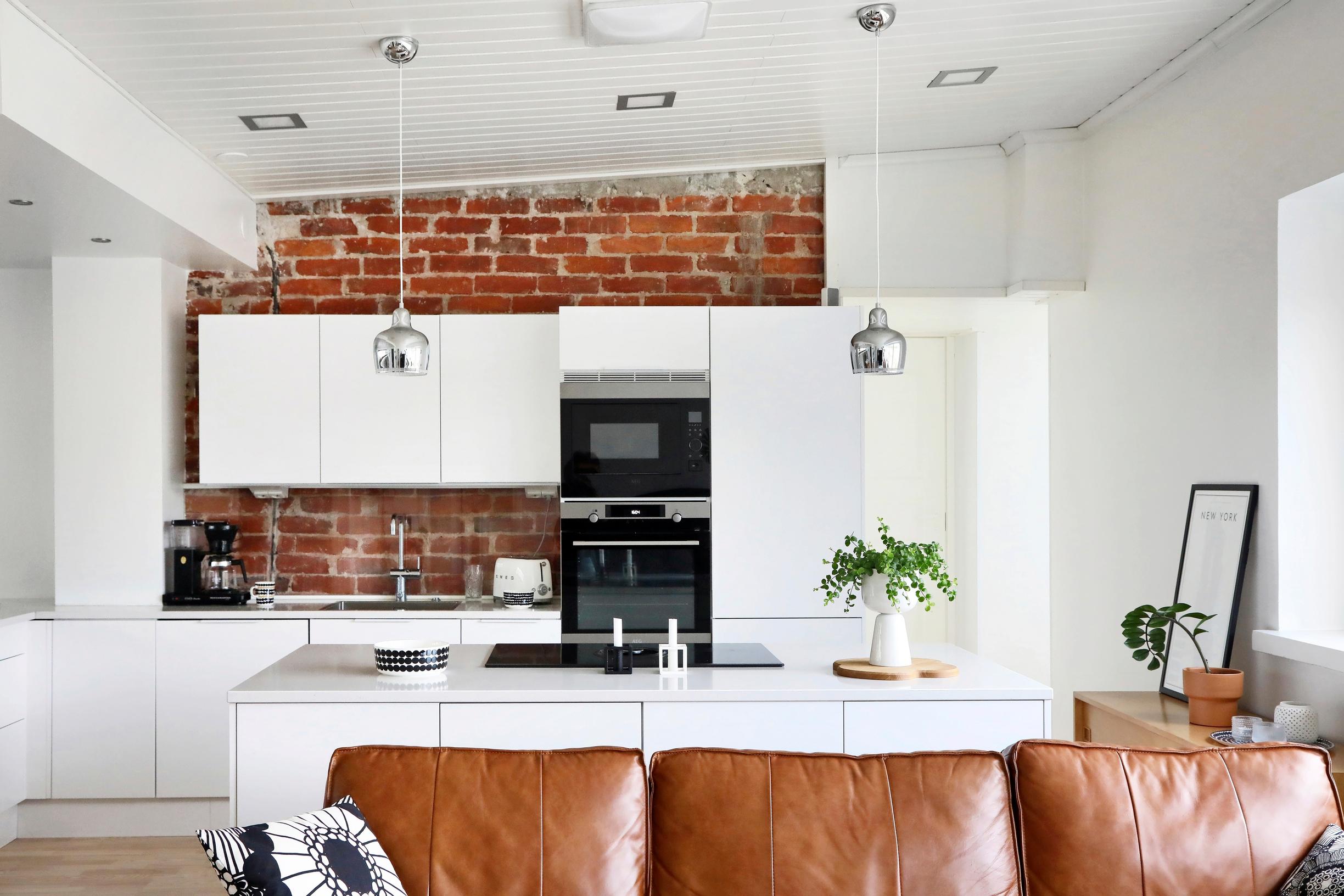 A modern white kitchen is set against an old red brick wall.