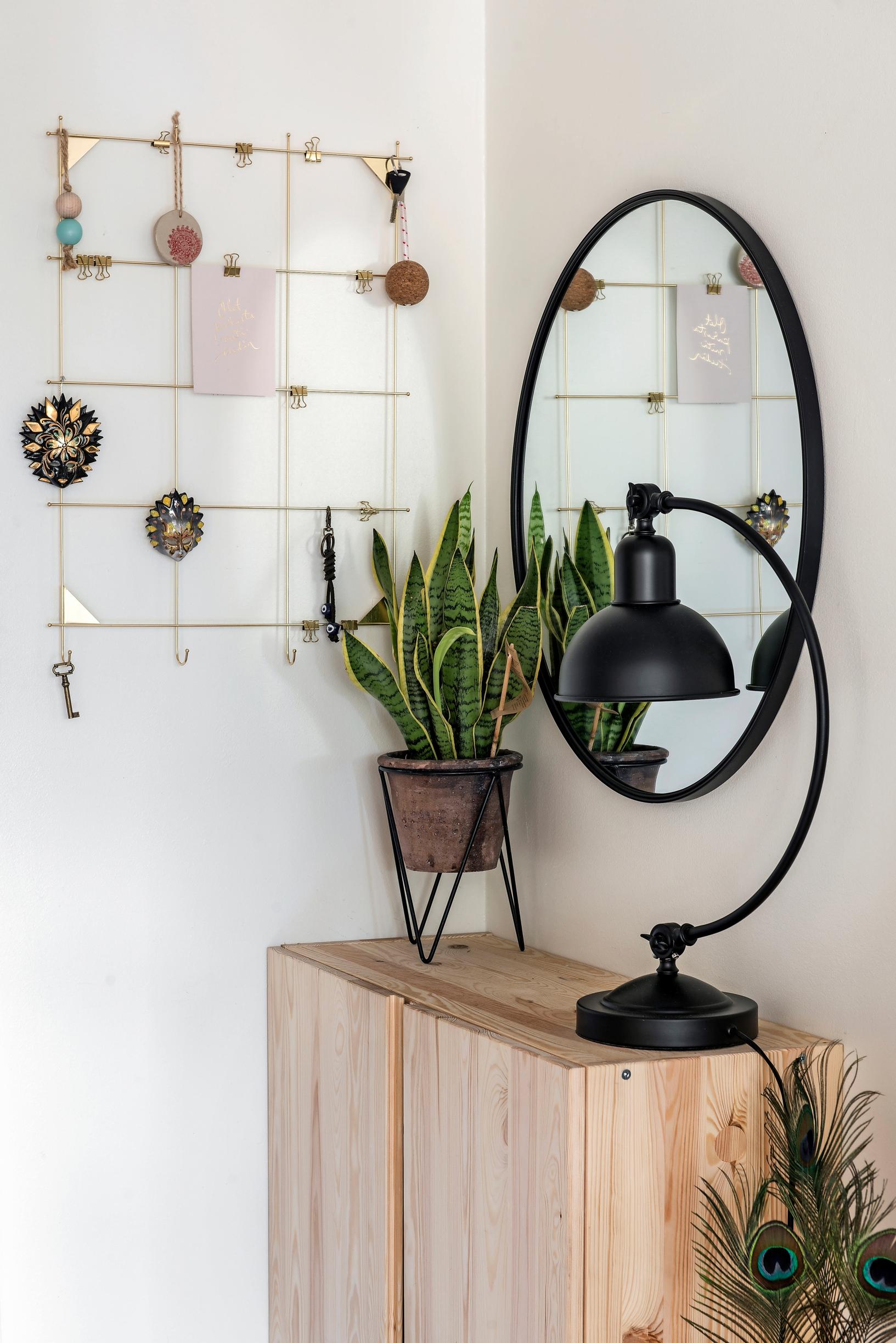 A round black-framed mirror, a snake plant, and a black table lamp atop a pine cabinet