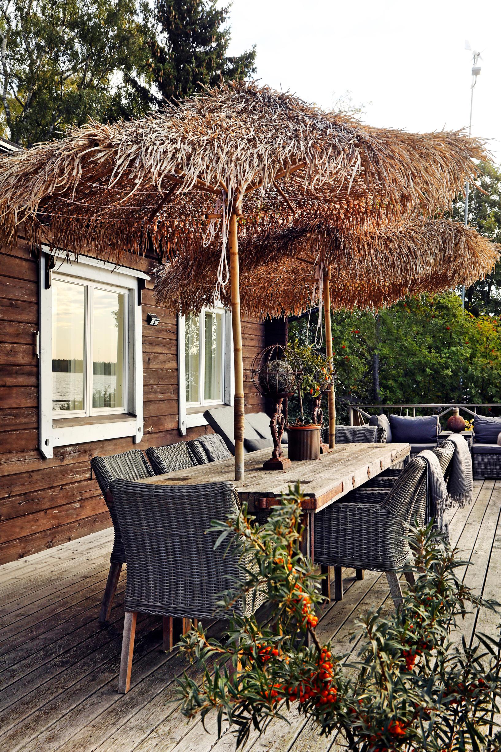 A table set on a terrace next to a log building, two fluffy sun umbrellas, sea buckthorn in the foreground.
