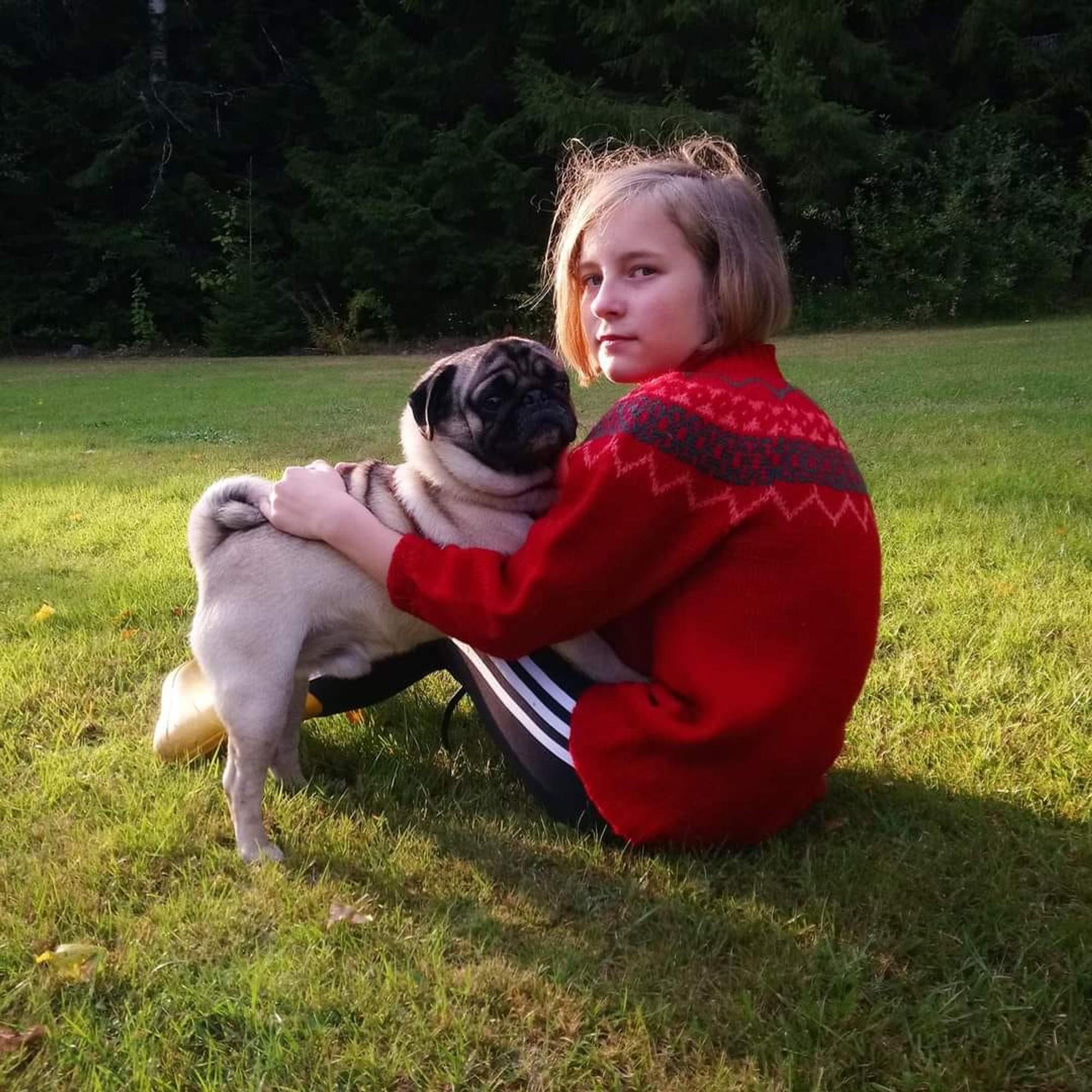 A girl wearing a sweater sits on grass holding a dog