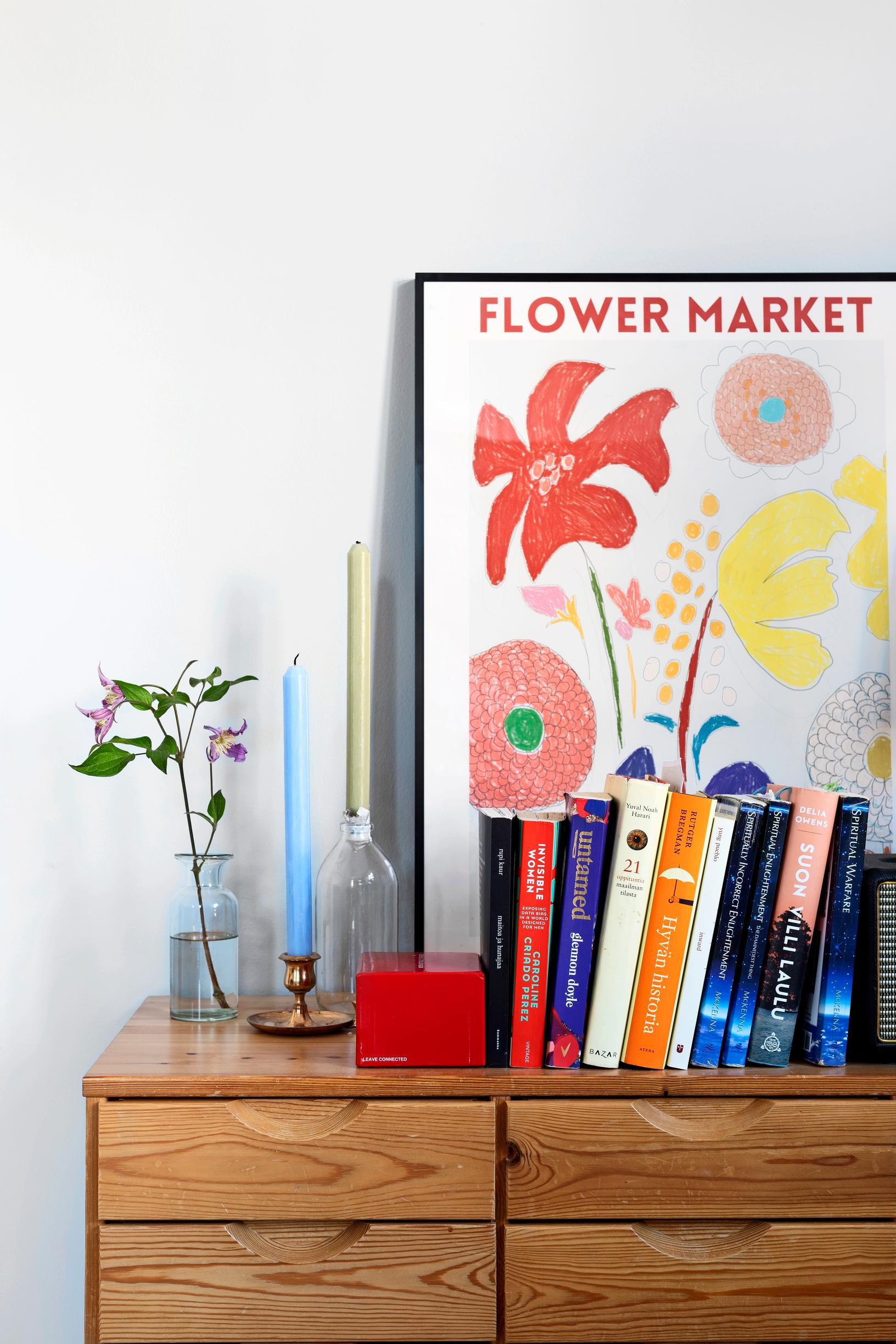 flower poster, books, candleholders, and a vase on a wooden dresser