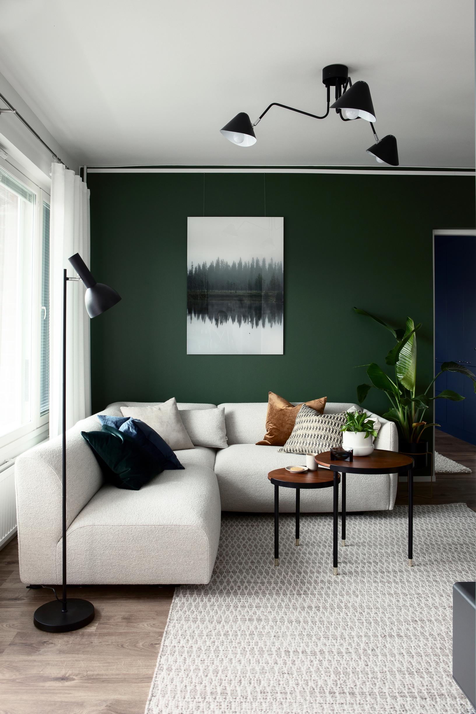 A white corner sofa is against a dark green wall. In front of the sofa is a brown nested table set.