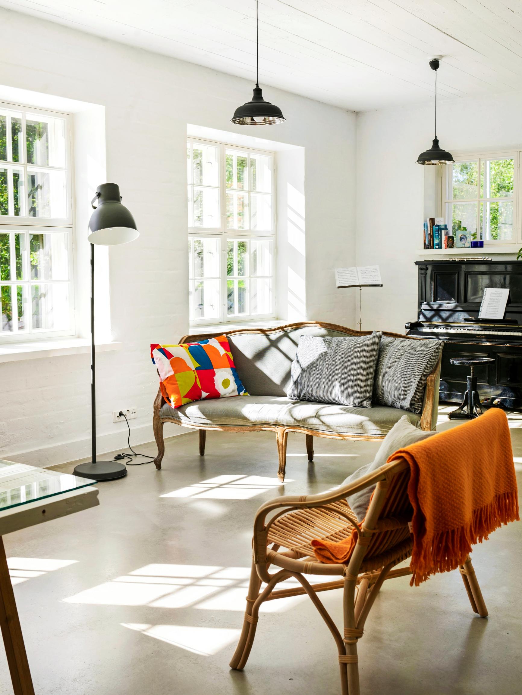 The white room features three multi-pane windows, a piano, and two lightweight sofas.