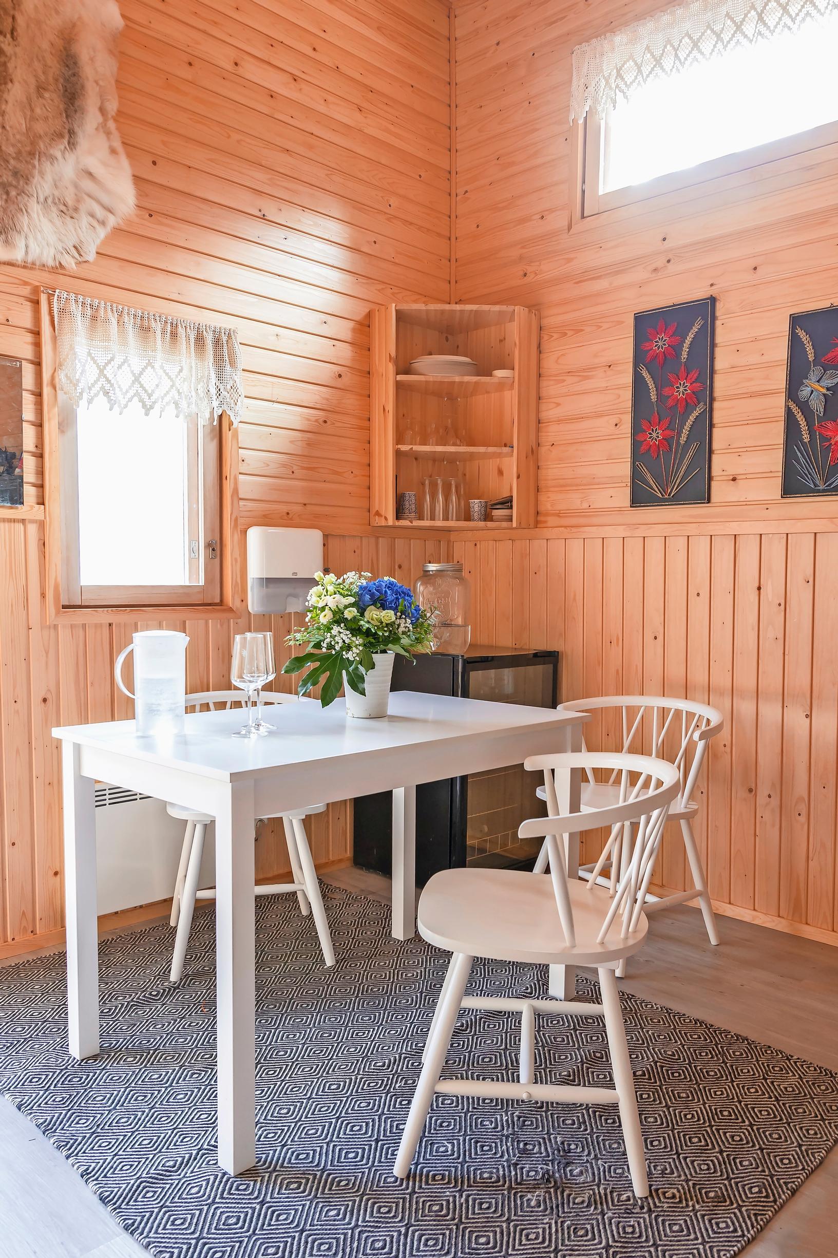 White dining set, blue rug, paintings, a window, and a corner cabinet