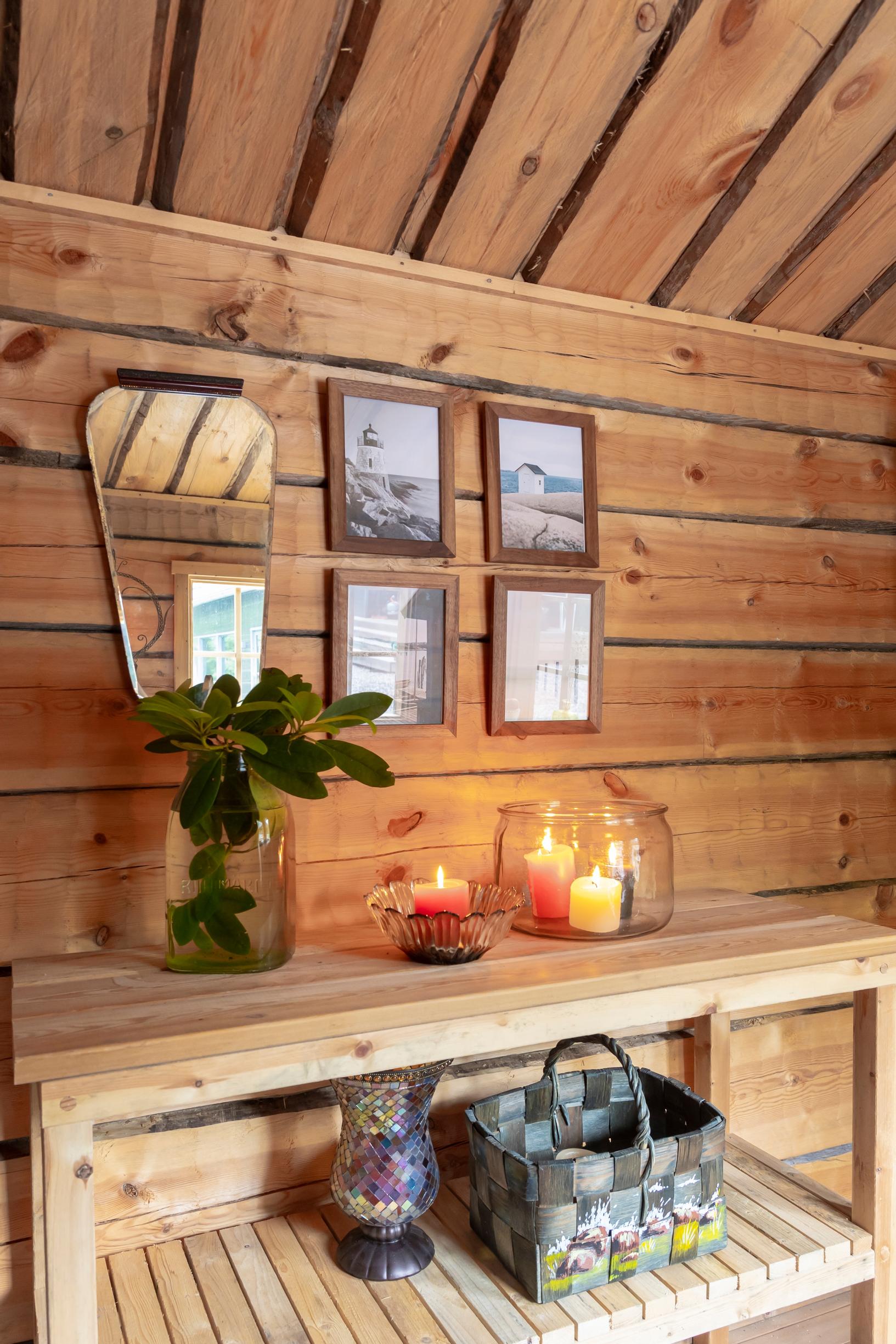 a mirror and paintings on a log wall, with candles on a shelf in the foreground