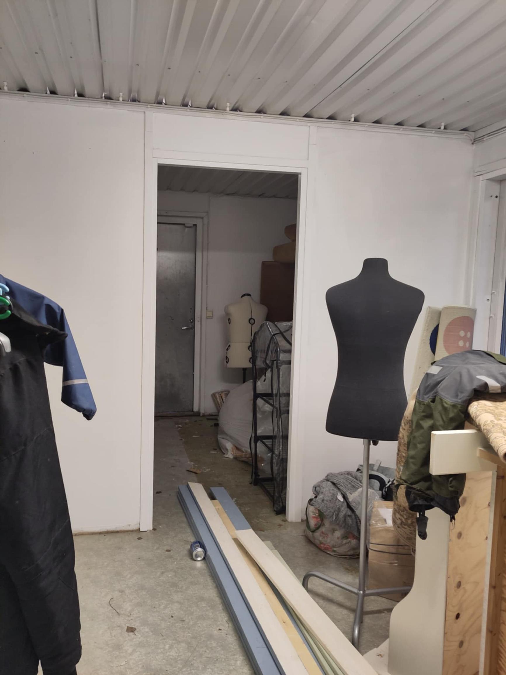 Inside the office container are two dress forms, clothes, and boards on the floor.