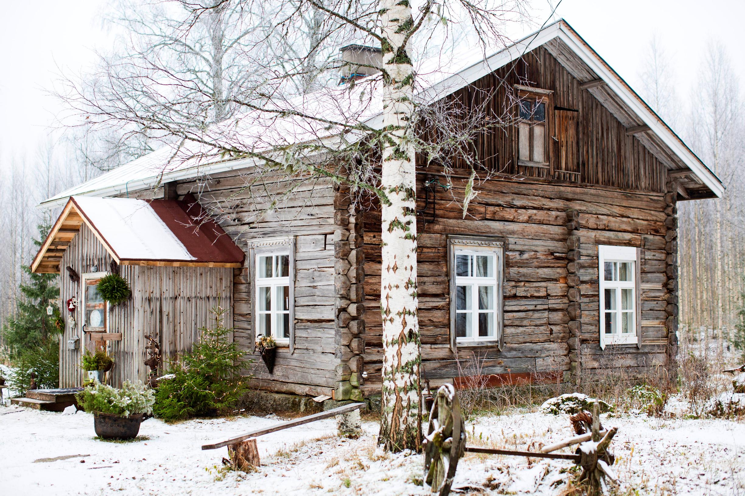 A gray log cottage in a winter landscape.