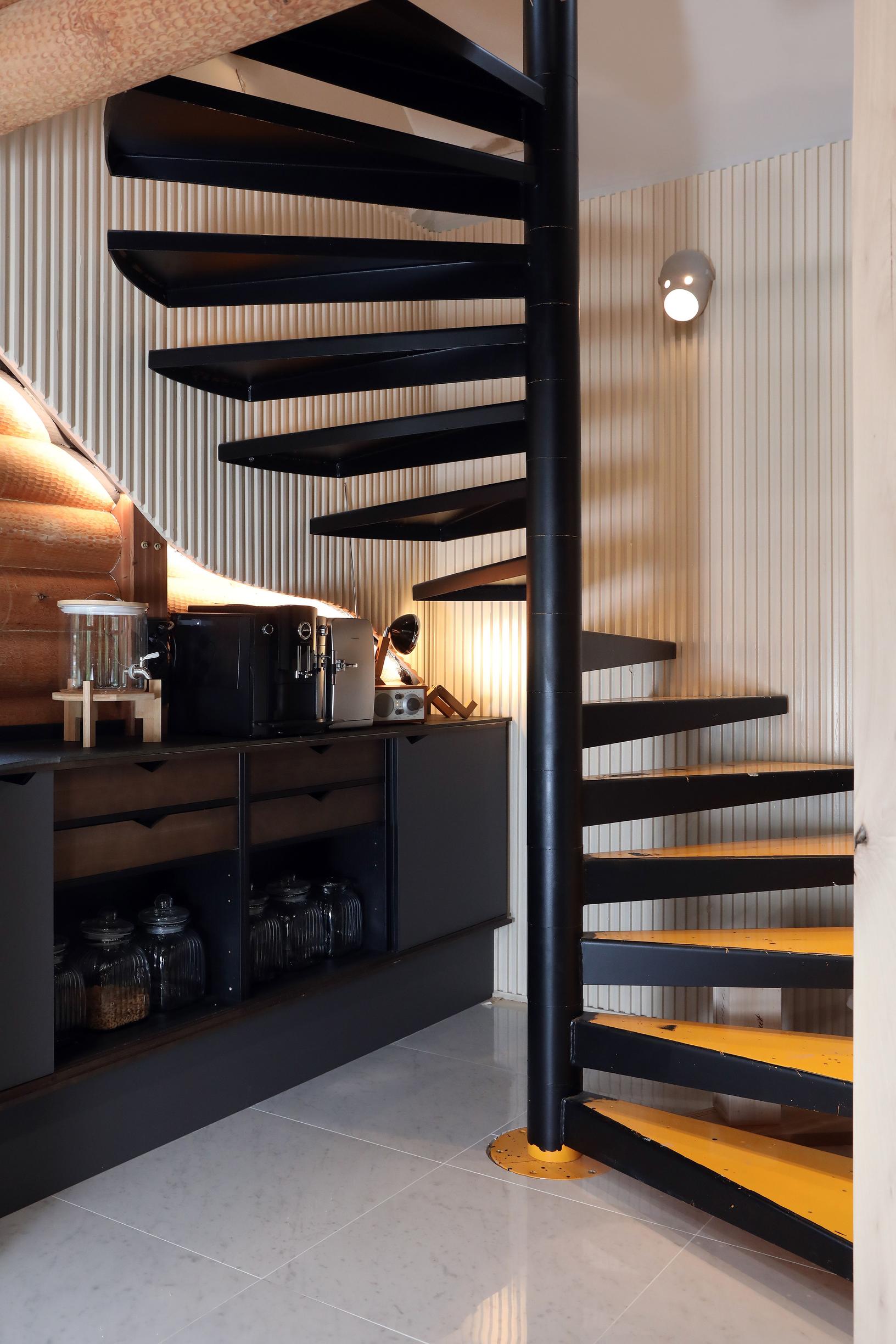 In the kitchen corner, there’s a dark spiral staircase with yellow steps.