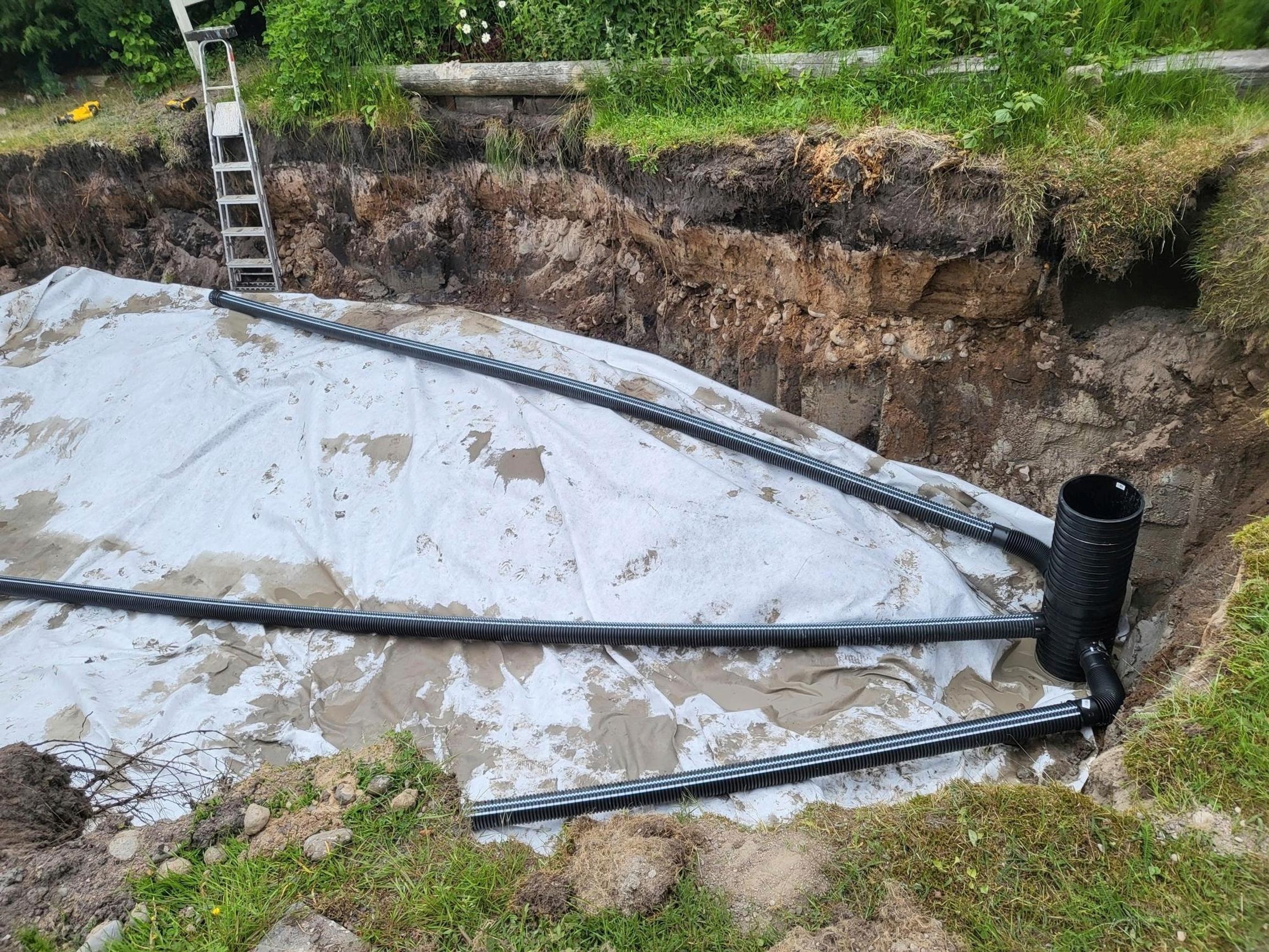 Pool plumbing installations at the bottom of the excavation, covered with fabric.
