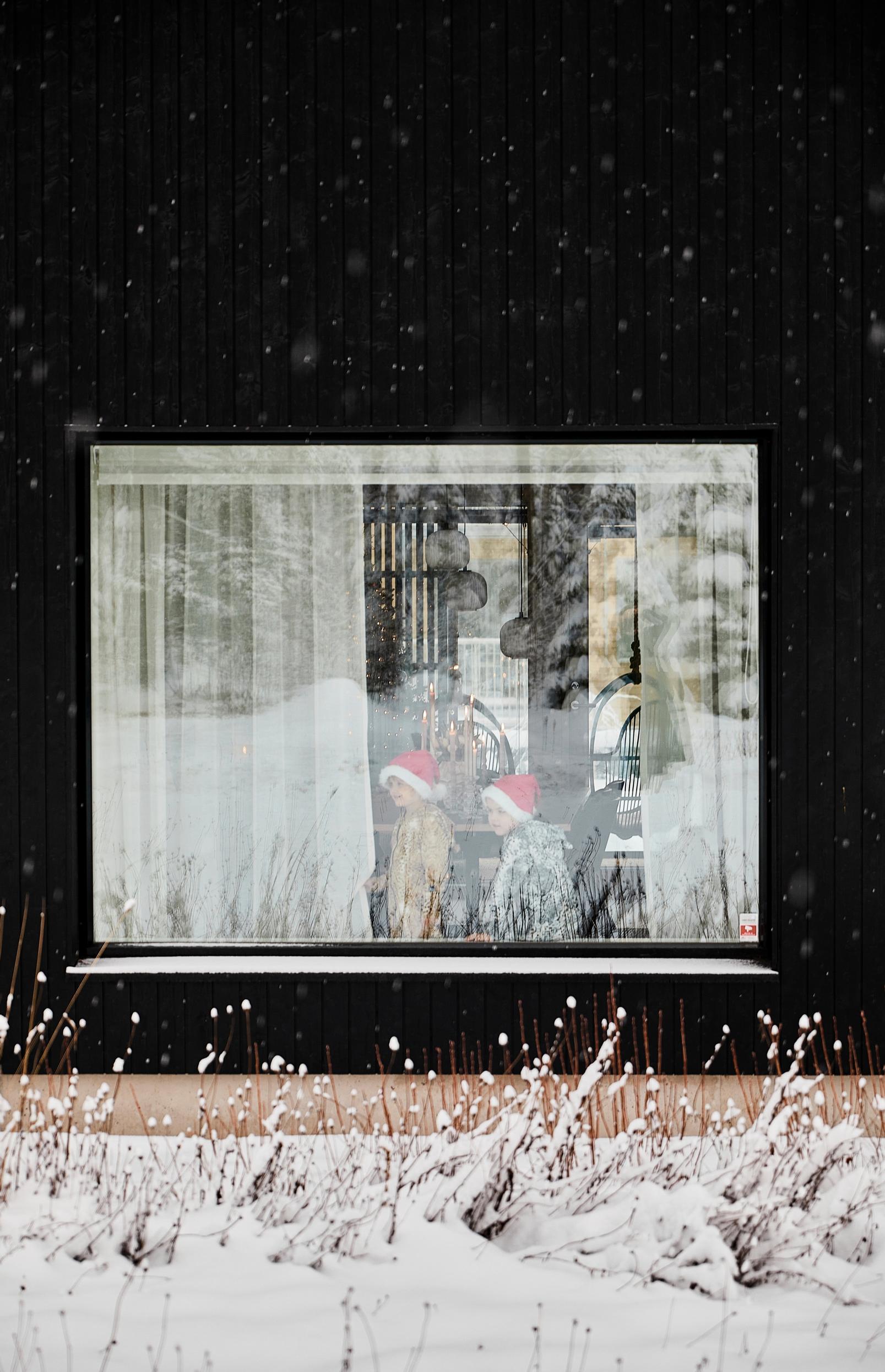 children wearing elf hats seen through a window in a black house
