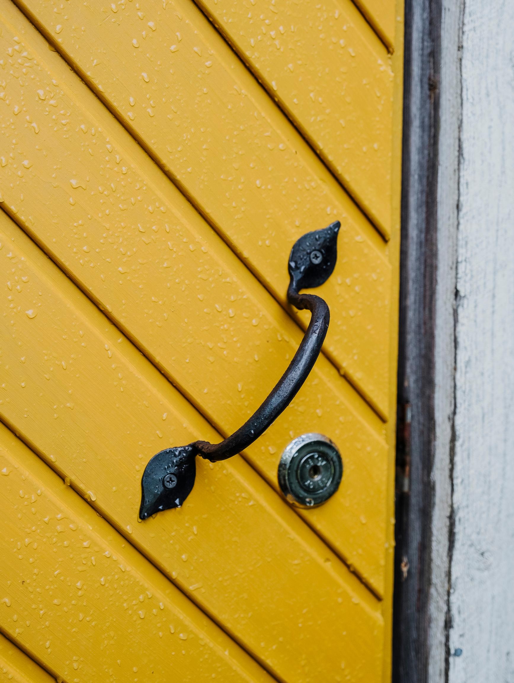 a yellow door with a black wrought-iron handle