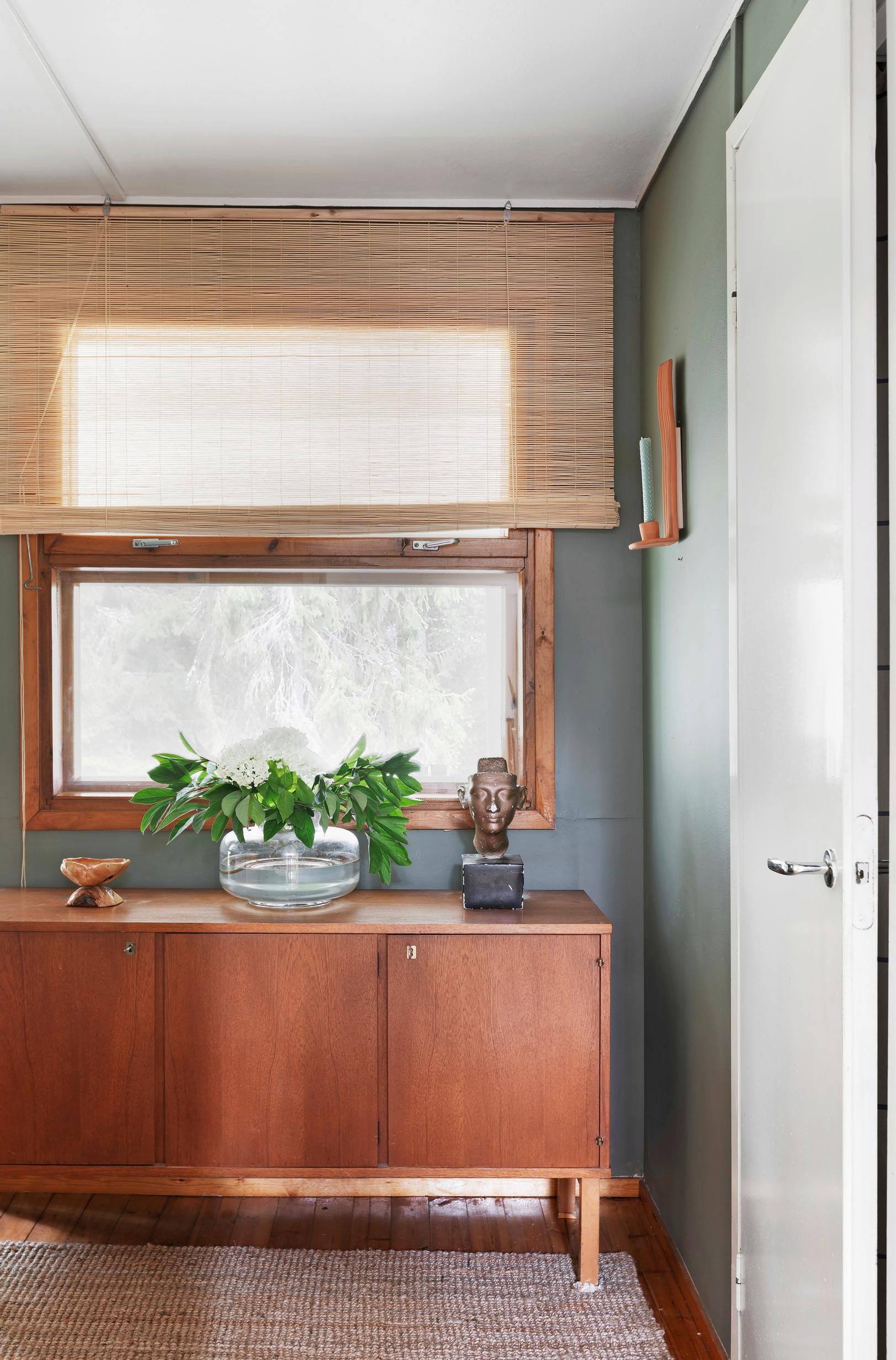 An old chest of drawers, flowers in a vase, a window, and a curtain.