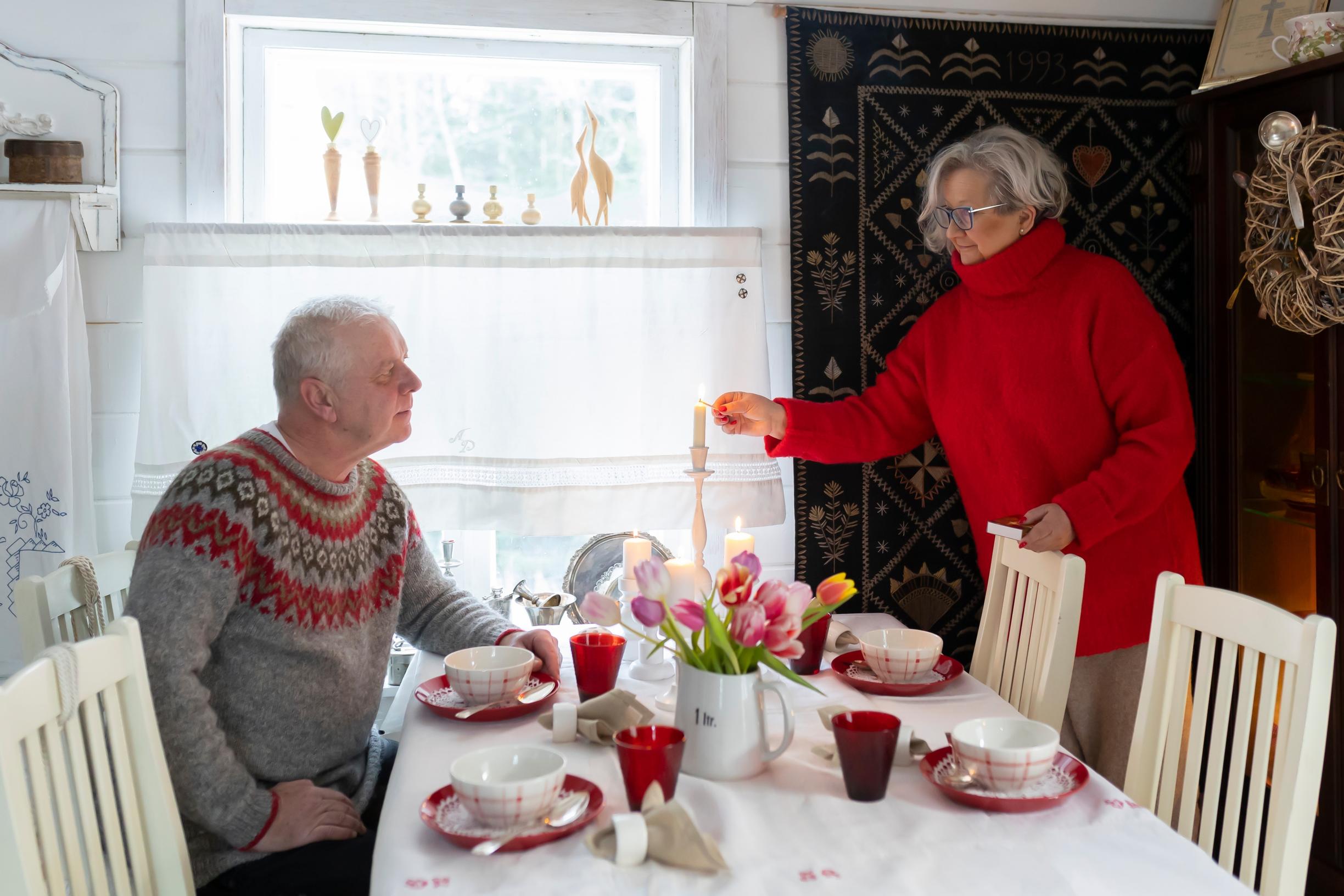 a man sits at a set dining table while a woman lights a candle