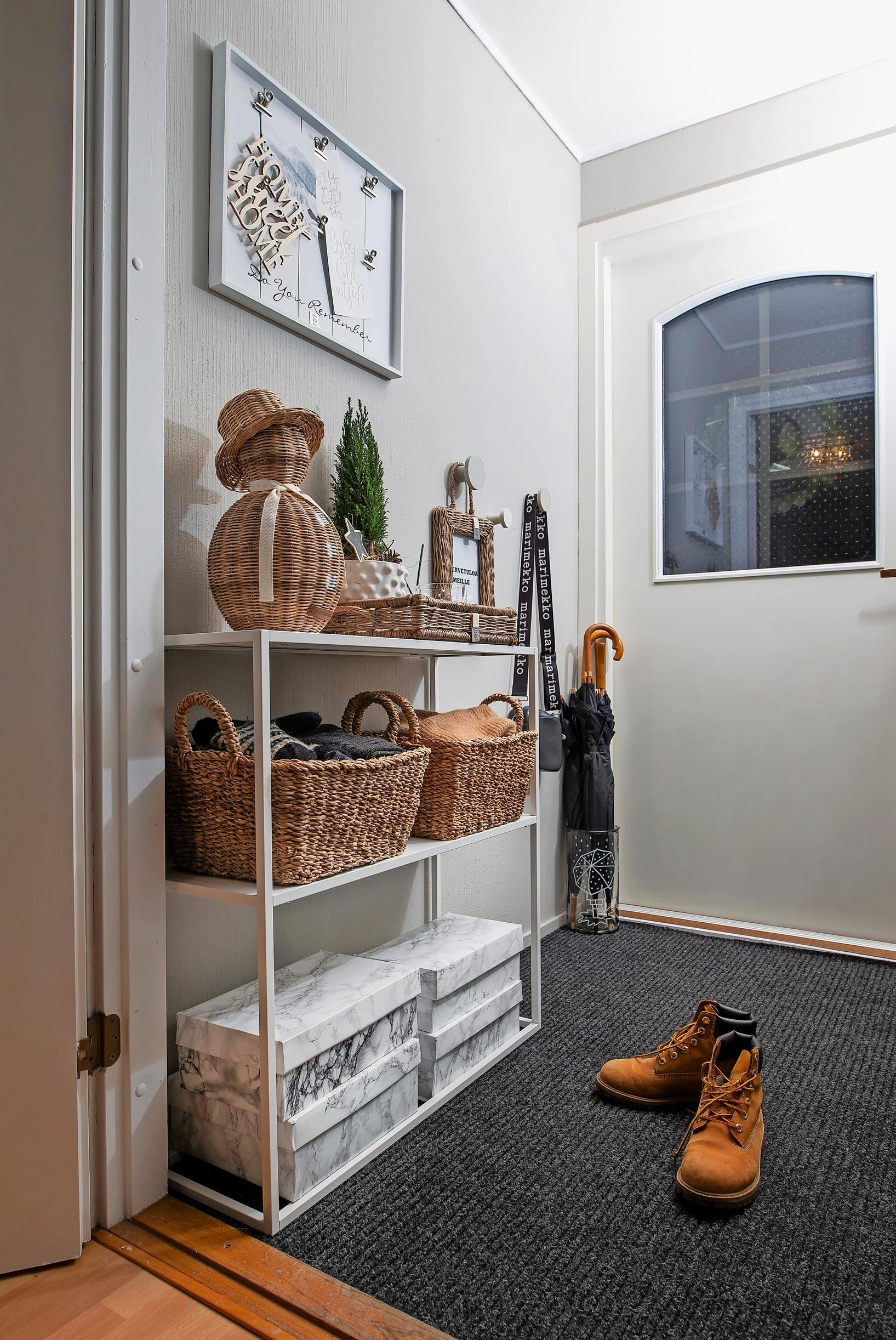A photo of an entryway with a shelf, storage boxes, and a gray rug by the front door.