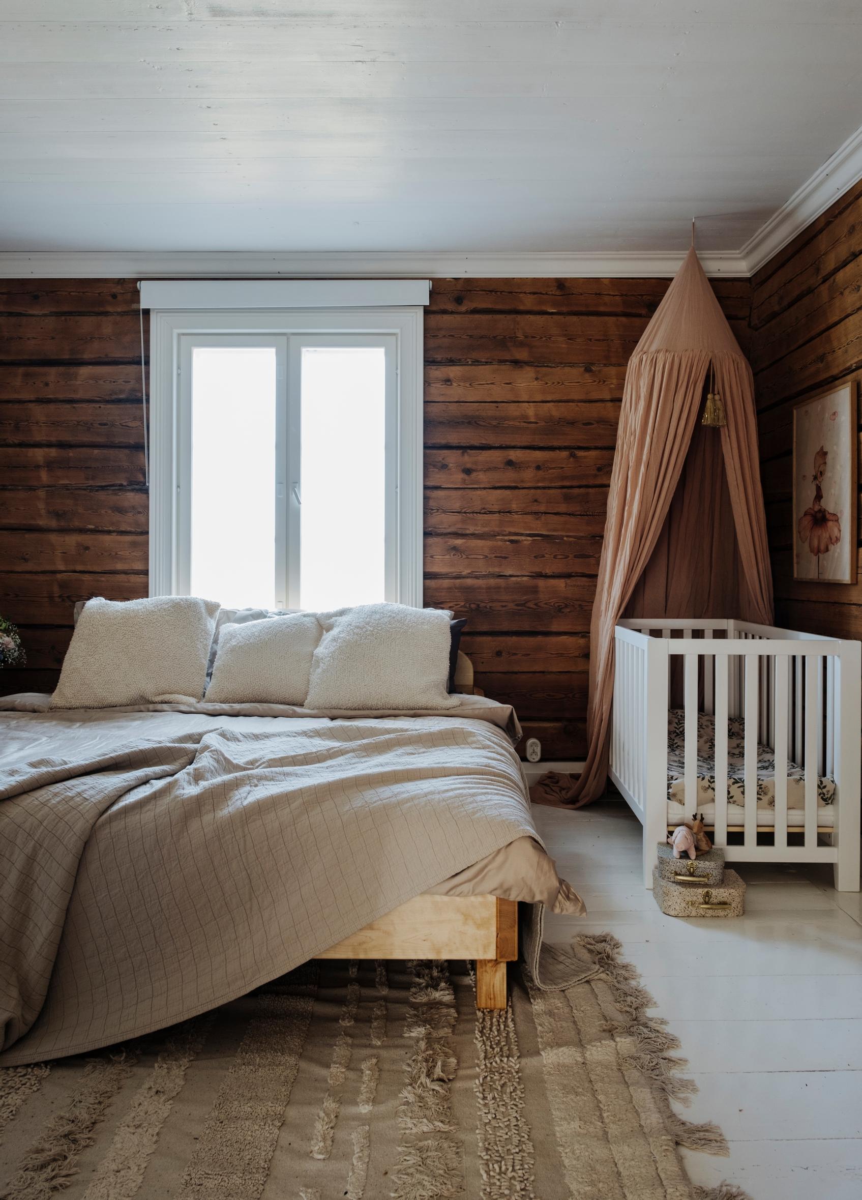 Log-walled bedroom with a crib with a canopy
