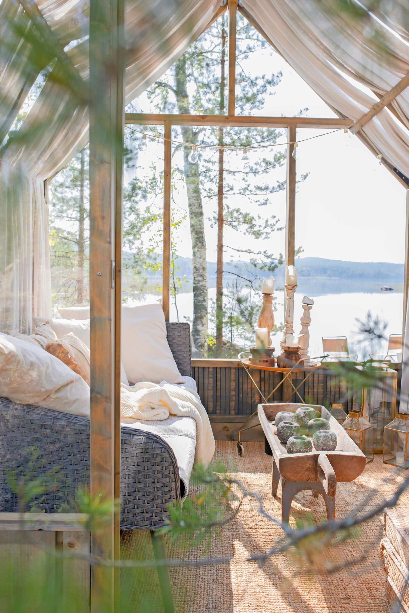 a sofa and a table with stone tealight holders in a glass-walled greenhouse