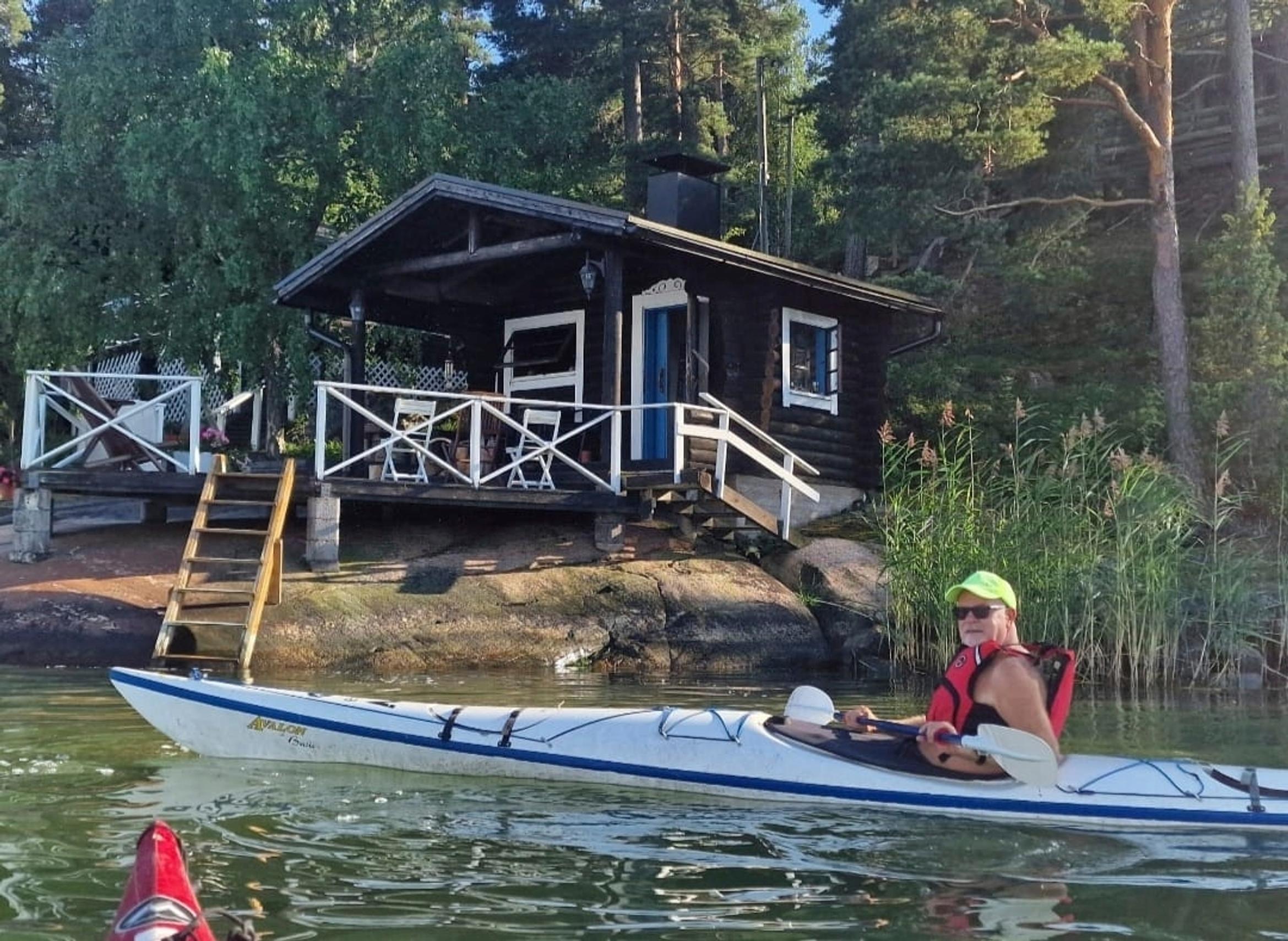 Singer Petri Laaksonen paddling, with the shoreline sauna in the background