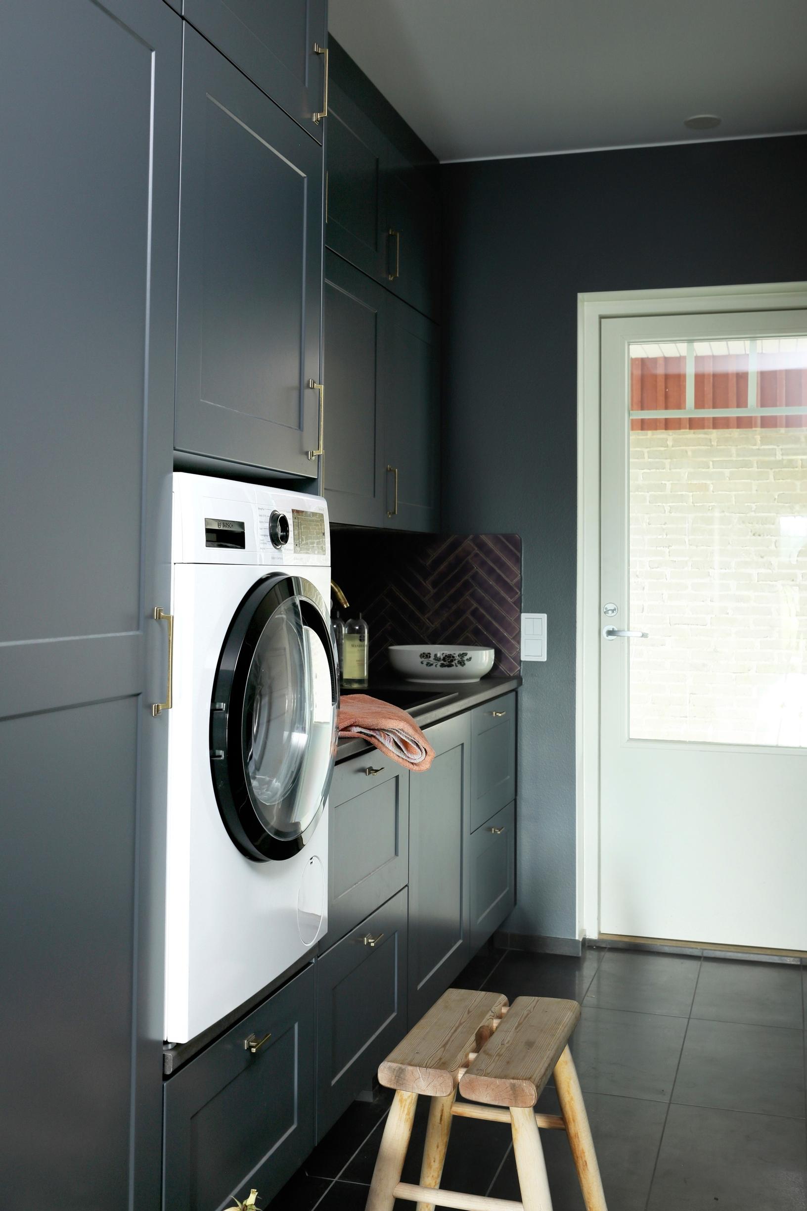 Utility room with gray cabinet doors. The washing machine is elevated about half a meter from the floor.