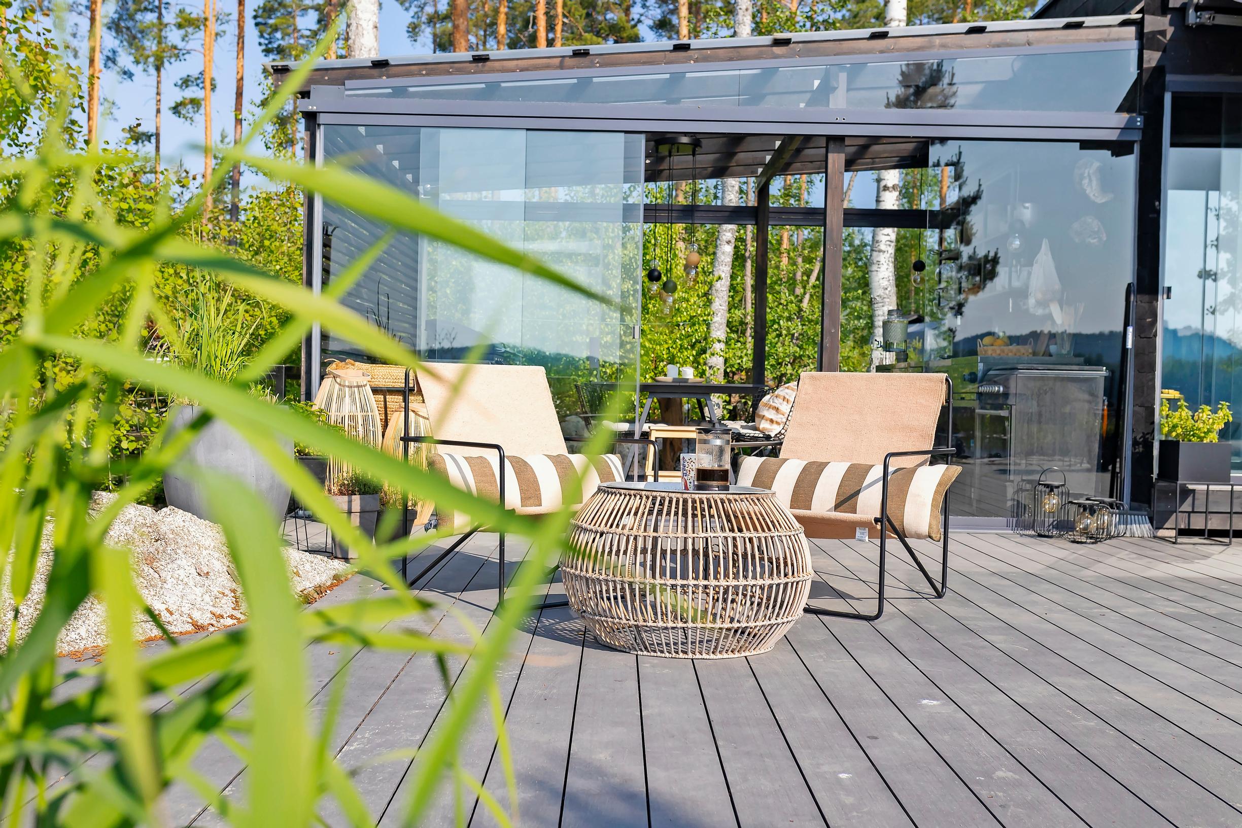 two garden chairs around a round rattan table, with a black glass-walled building in the background