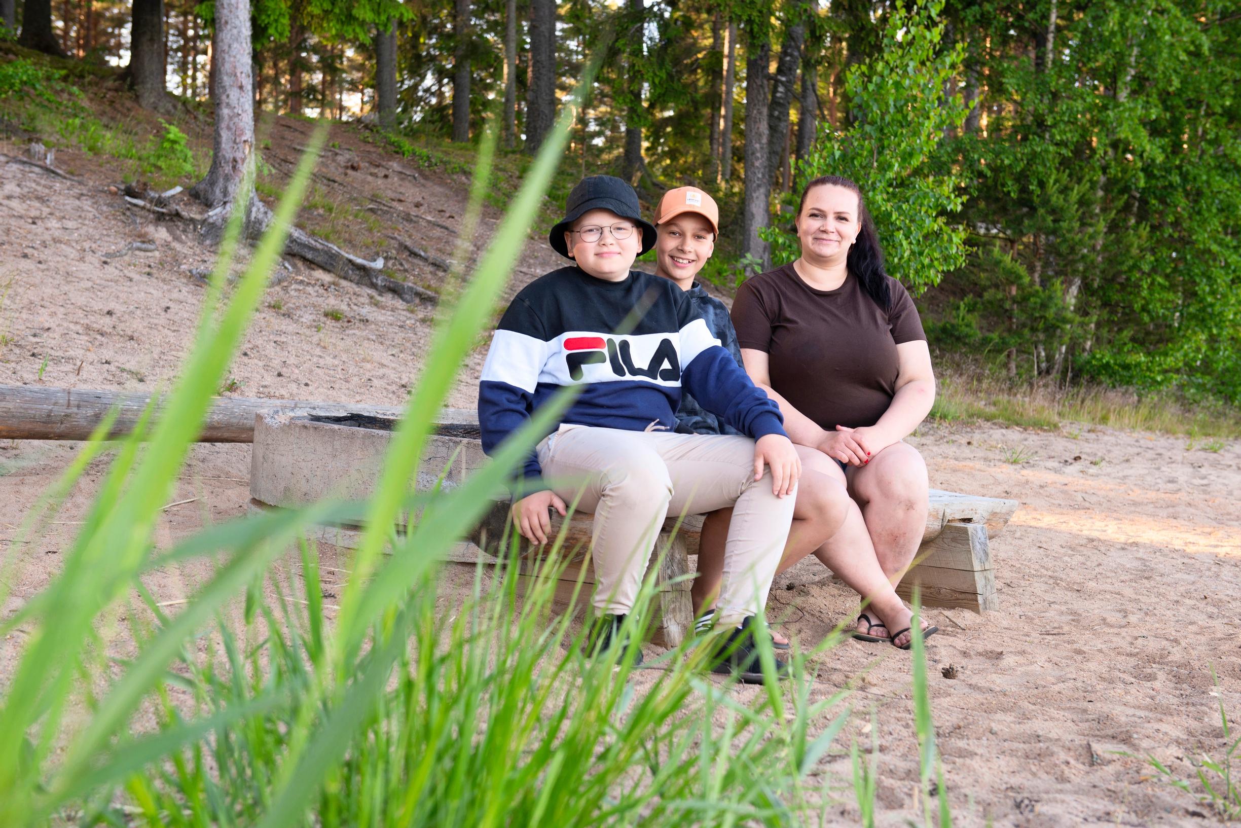 a mother and two boys sitting on a bench on a sandy beach
