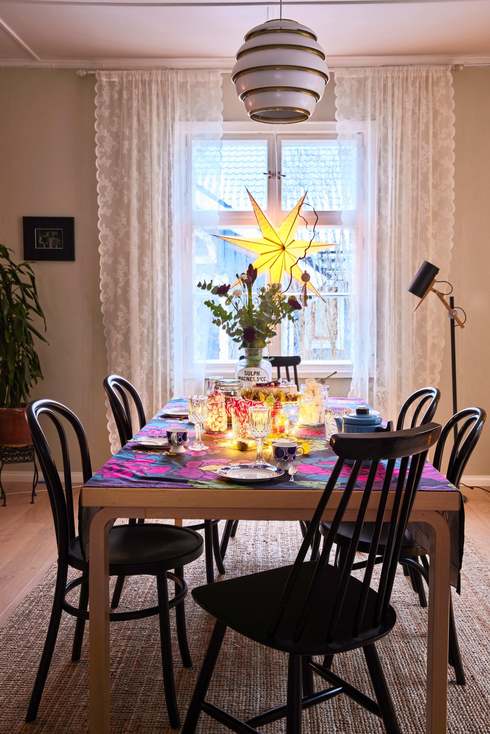 Dining table with a colorful tablecloth and surrounded by black Viennese chairs
