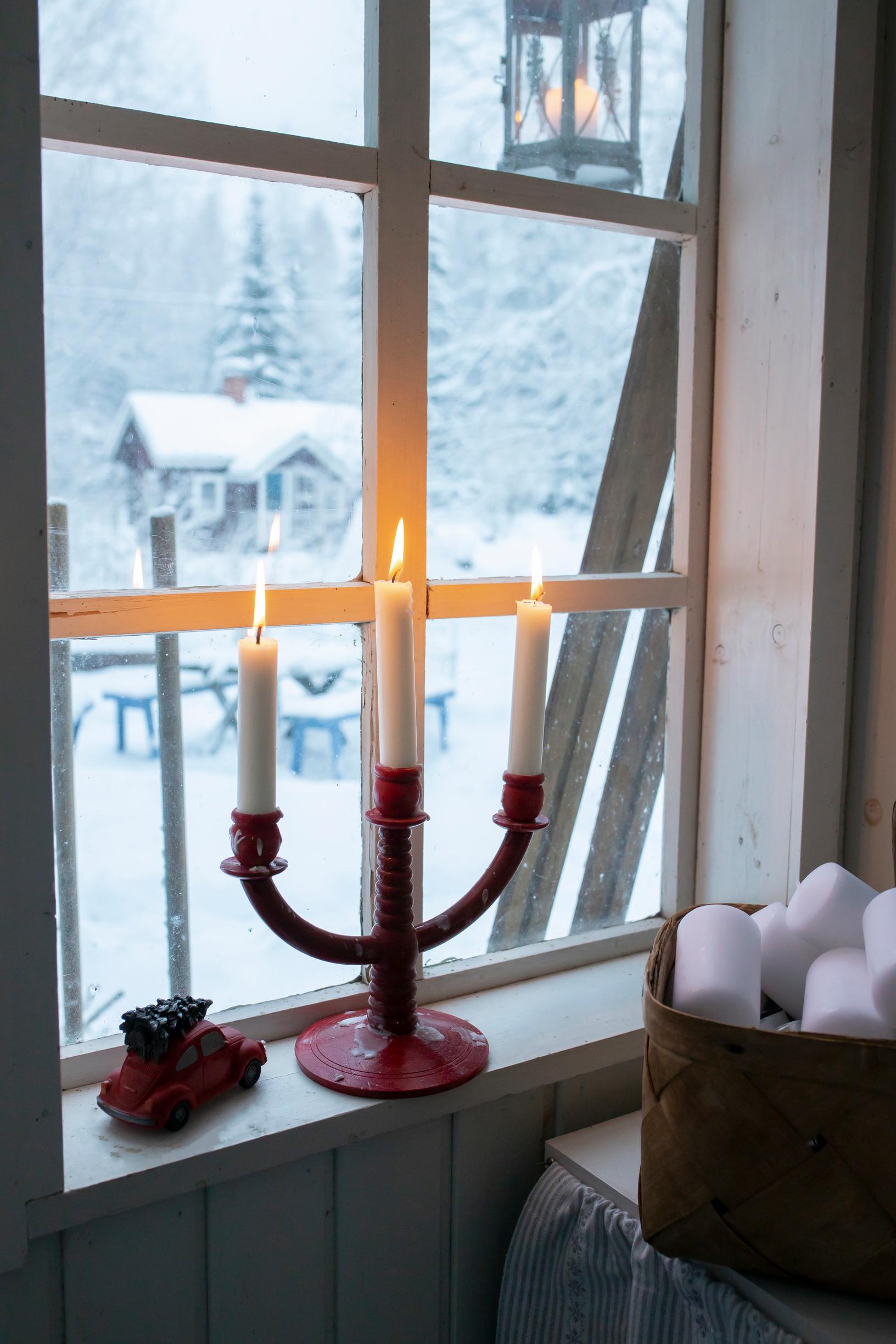 A candelabra in the window with a snowy view outside.