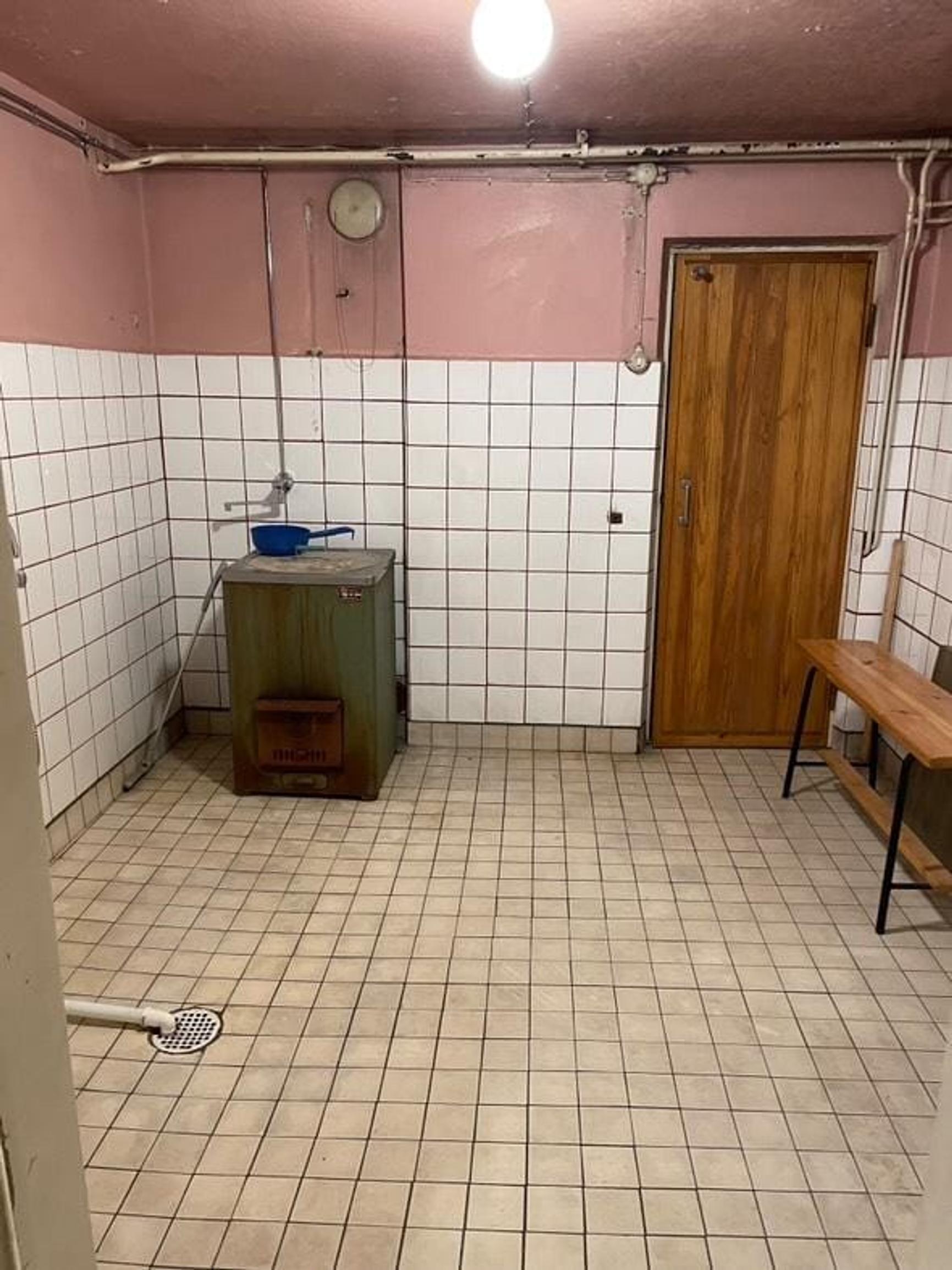 The bathroom has a brownish tiled floor, white-tiled walls up to about waist height, and pale pink paint on the upper parts of the walls.