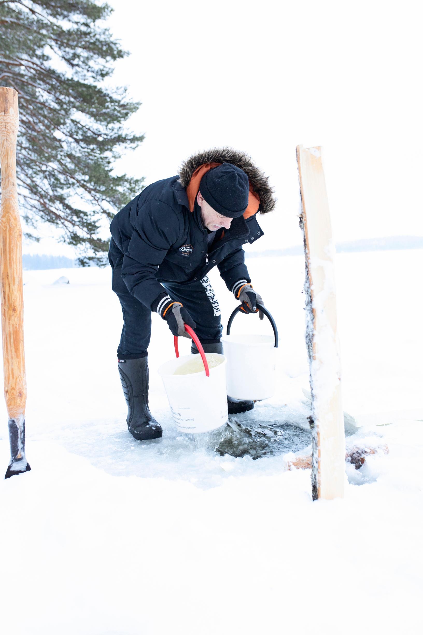 A man lifts two buckets of water from an ice hole.
