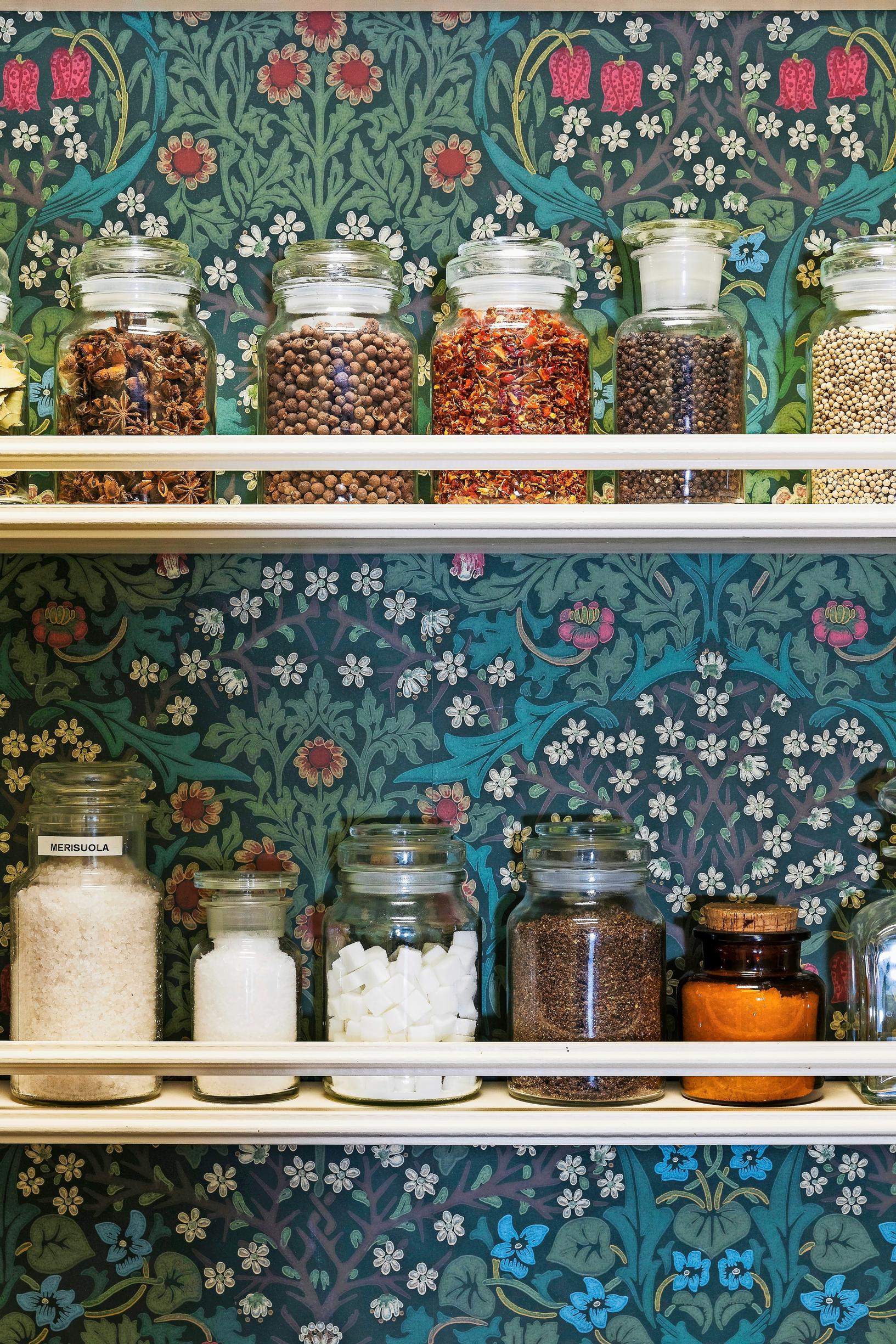 A wallpaper-backed pantry with glass jars on the shelf