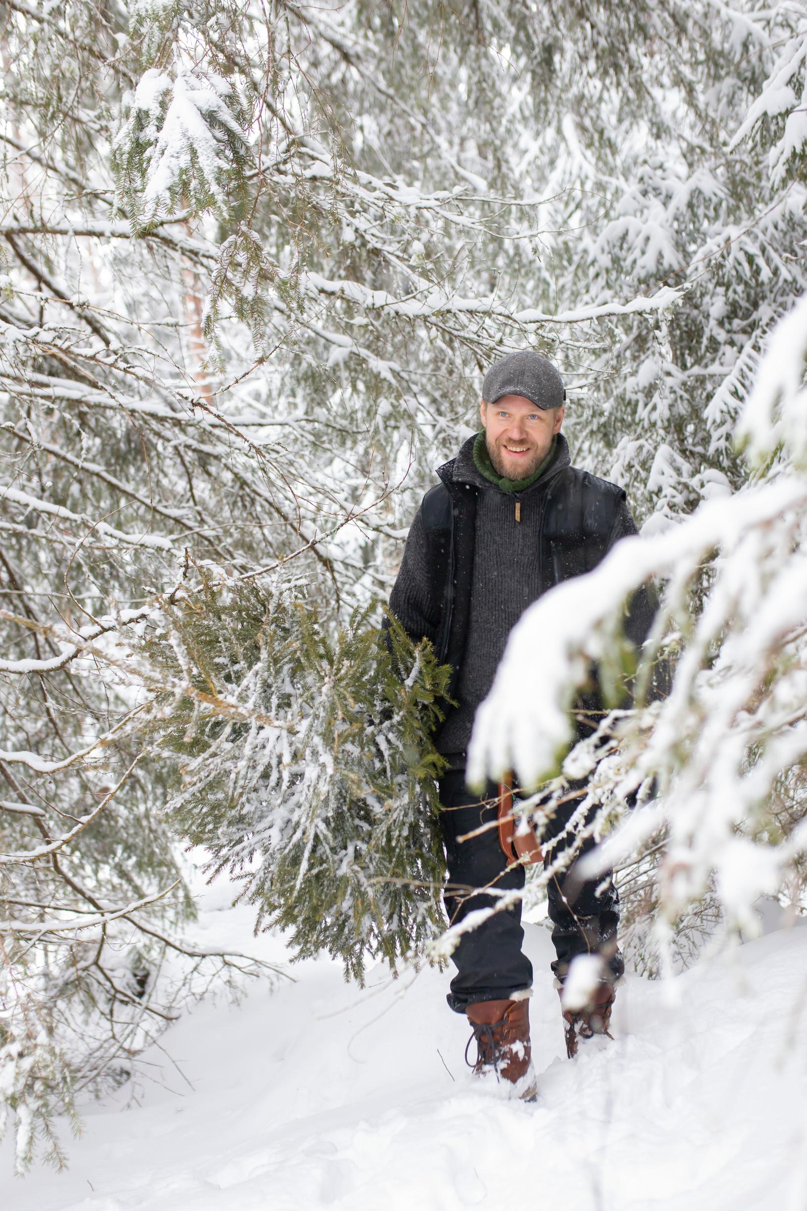A man carrying a Christmas tree in a snowy forest.