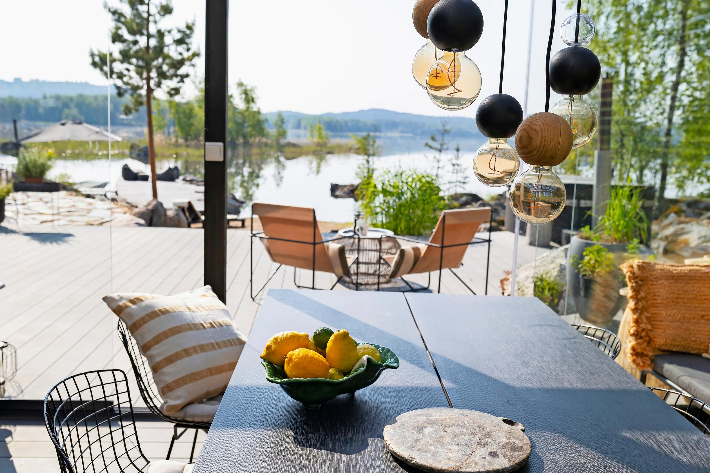 a dining set on the terrace, lemons in a bowl, a hanging light, and the lake in the background