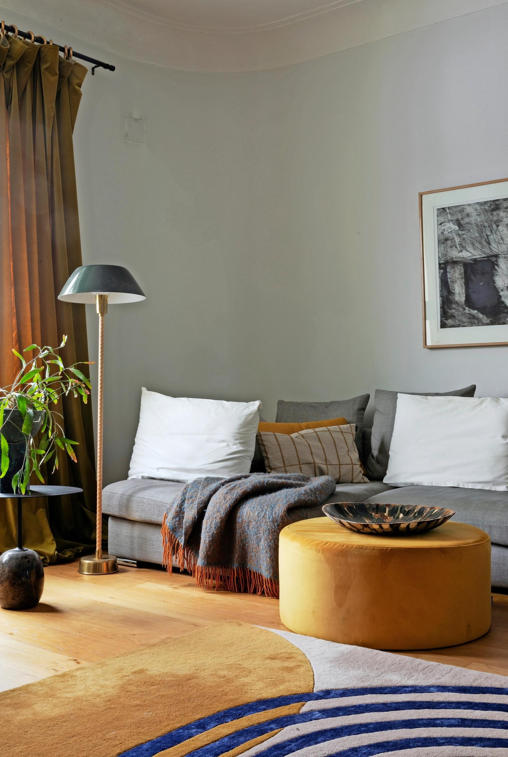 A sofa against the wall with numerous pillows, plus an ottoman and a floor lamp.