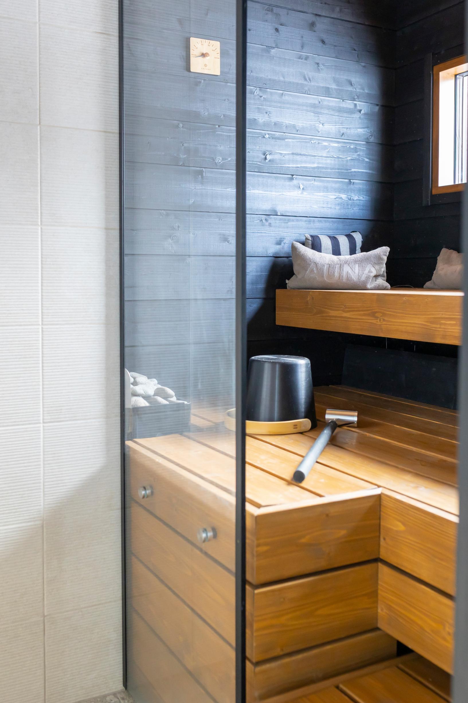 Thick wooden beams as sauna benches in a modern sauna with a black wall, sauna bucket, and sauna pillows