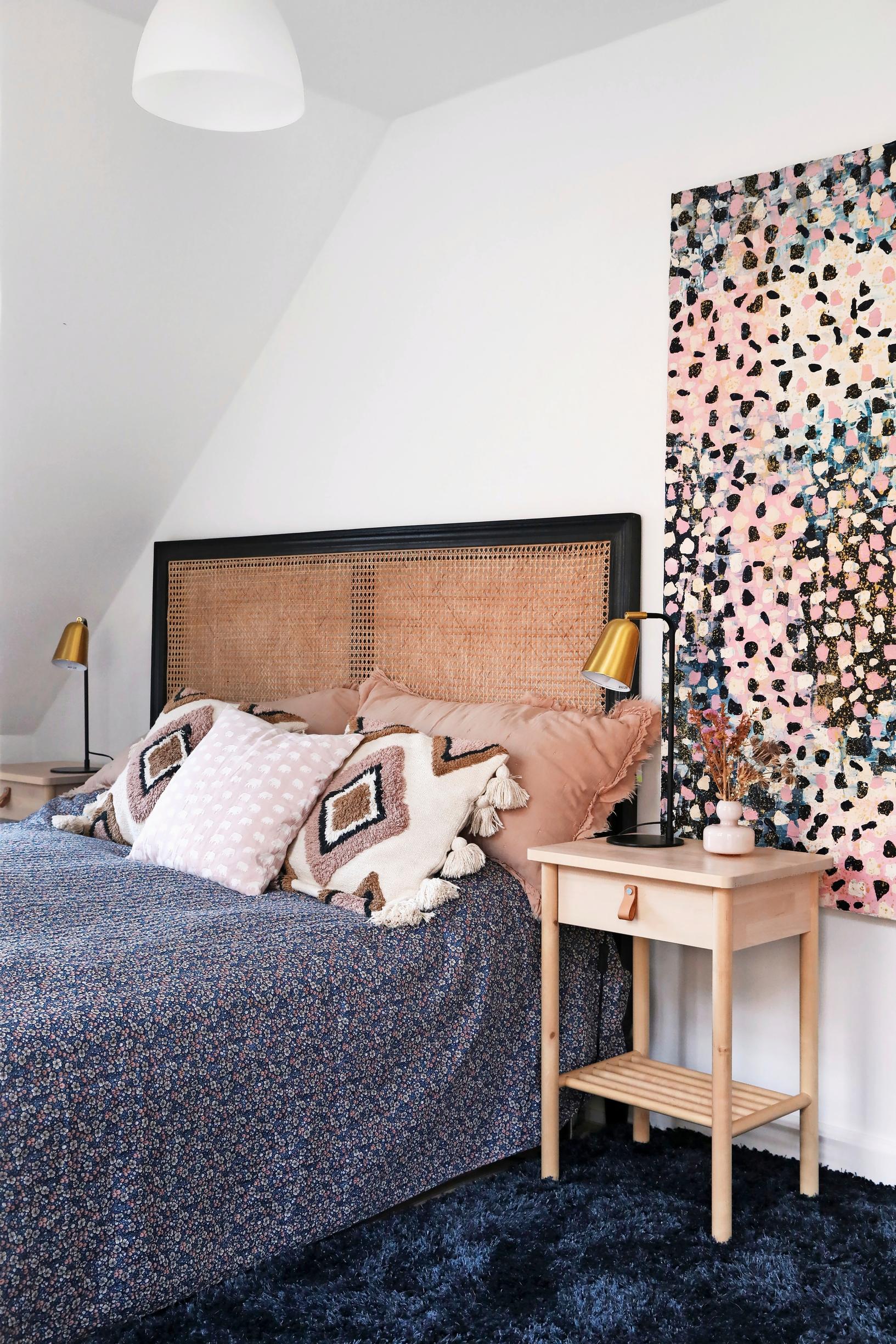 In the bedroom, a rattan headboard and a painting by the resident
