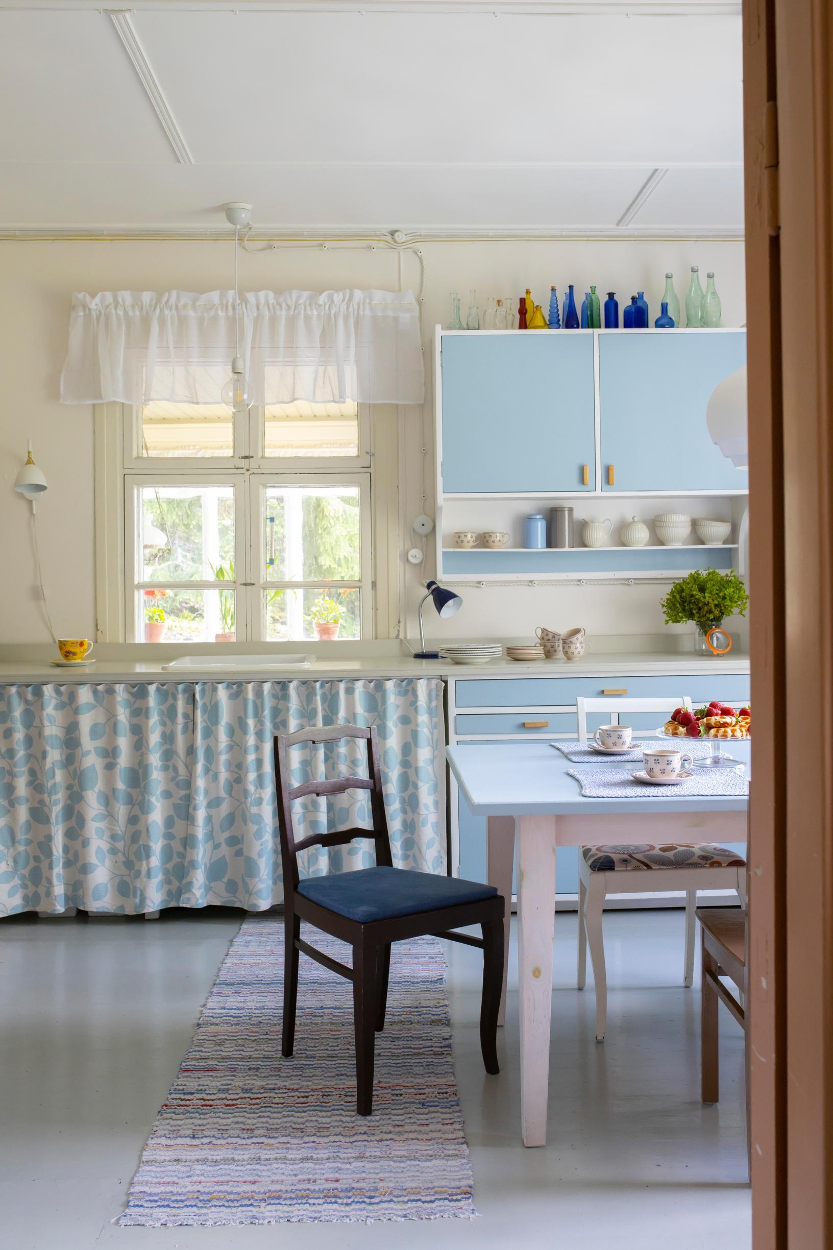 A beautiful old farmhouse kitchen with a traditional dish cabinet. Under the window, additional storage space was added to the lower cabinets, covered by a fabric curtain.