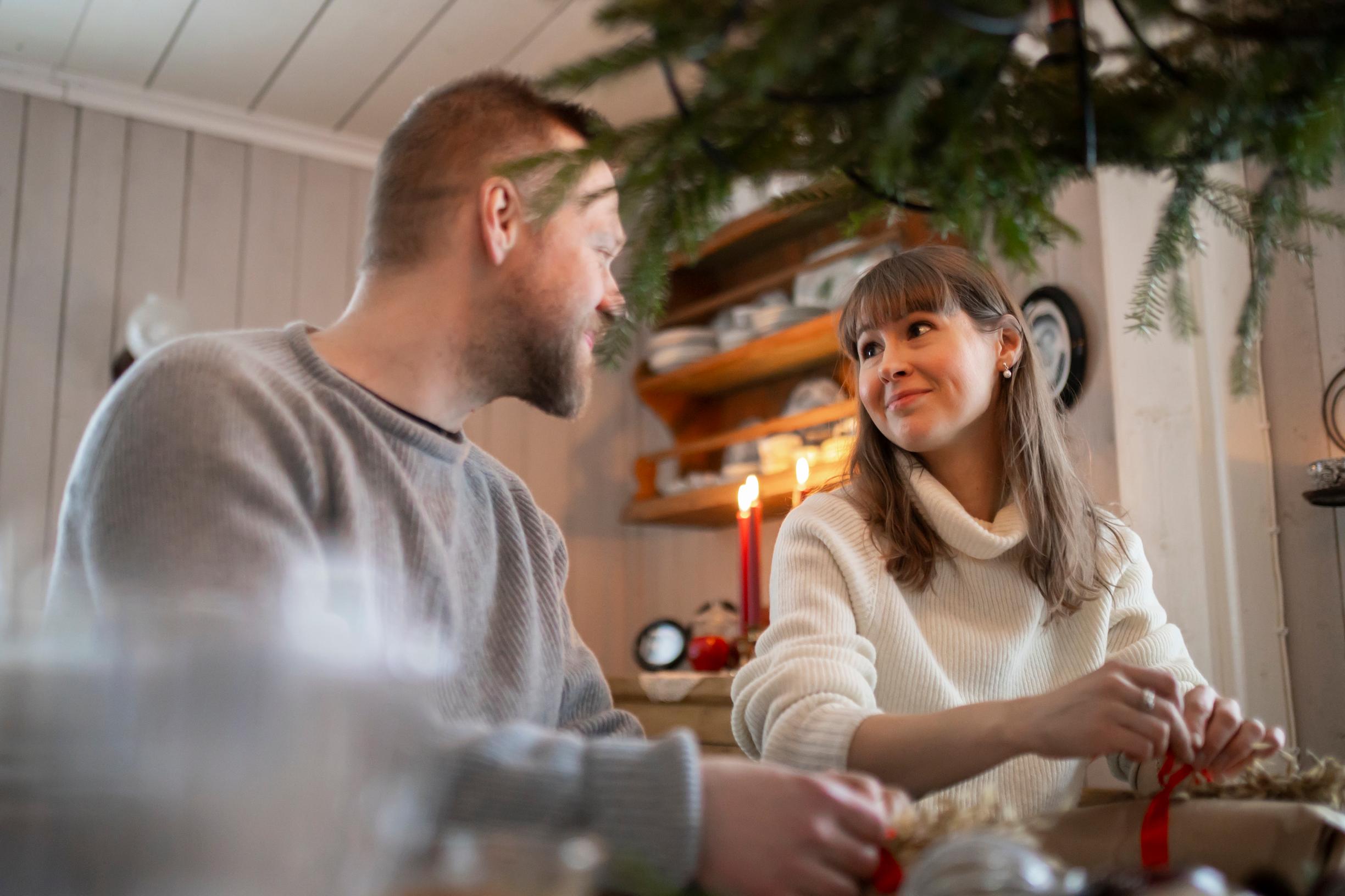 The couple looks at each other while sitting at a table wrapping Christmas gifts.