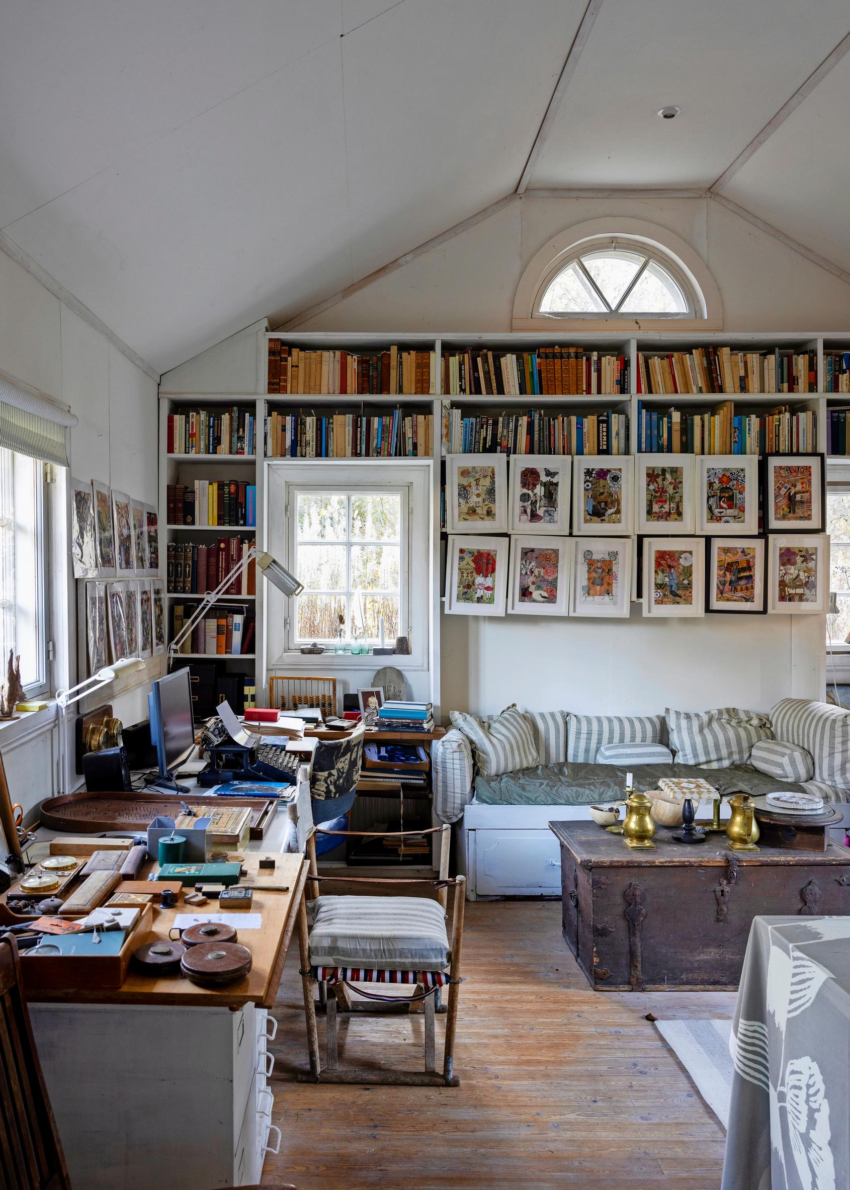 Studio with many shelves and books. A desk stands in front of the window.